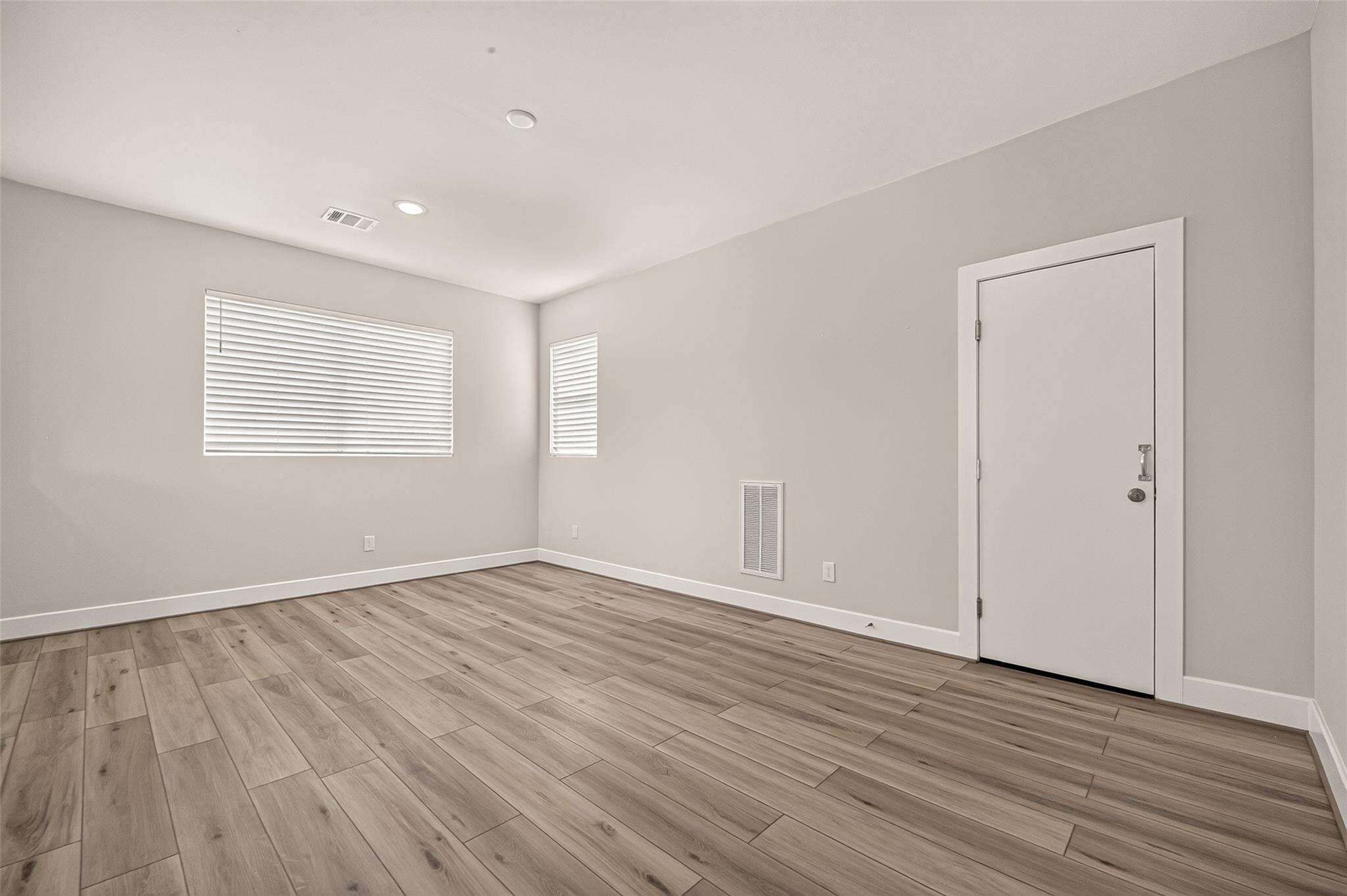 Empty room with wood-look plank flooring, two windows with blinds, and a white door.