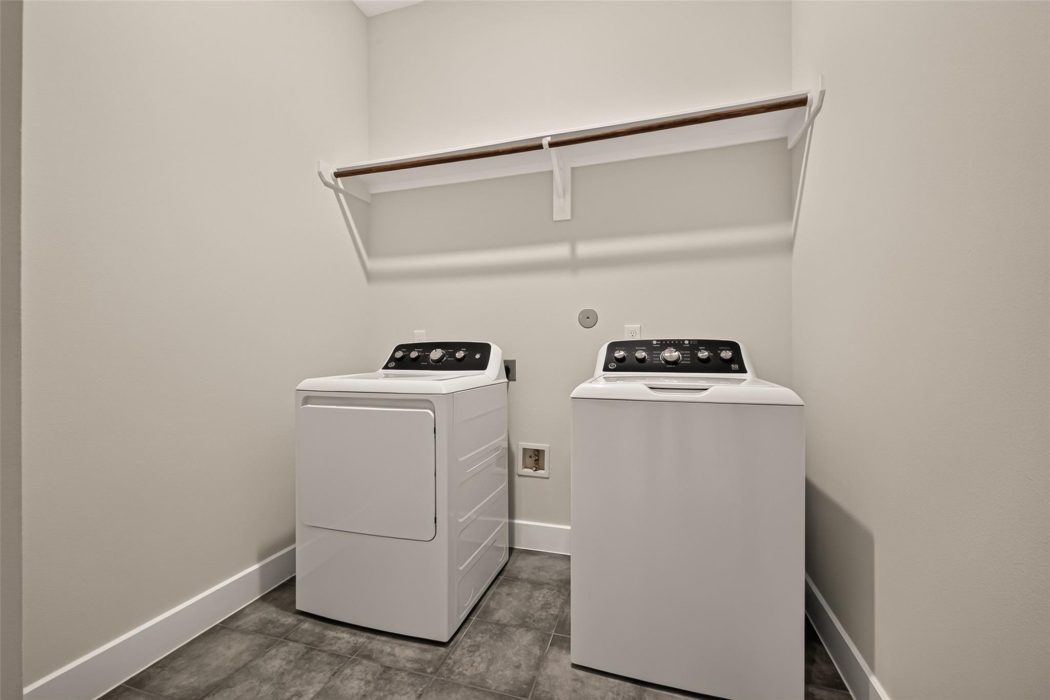 Laundry room with white washer and dryer beneath an overhead shelf and hanging rod.