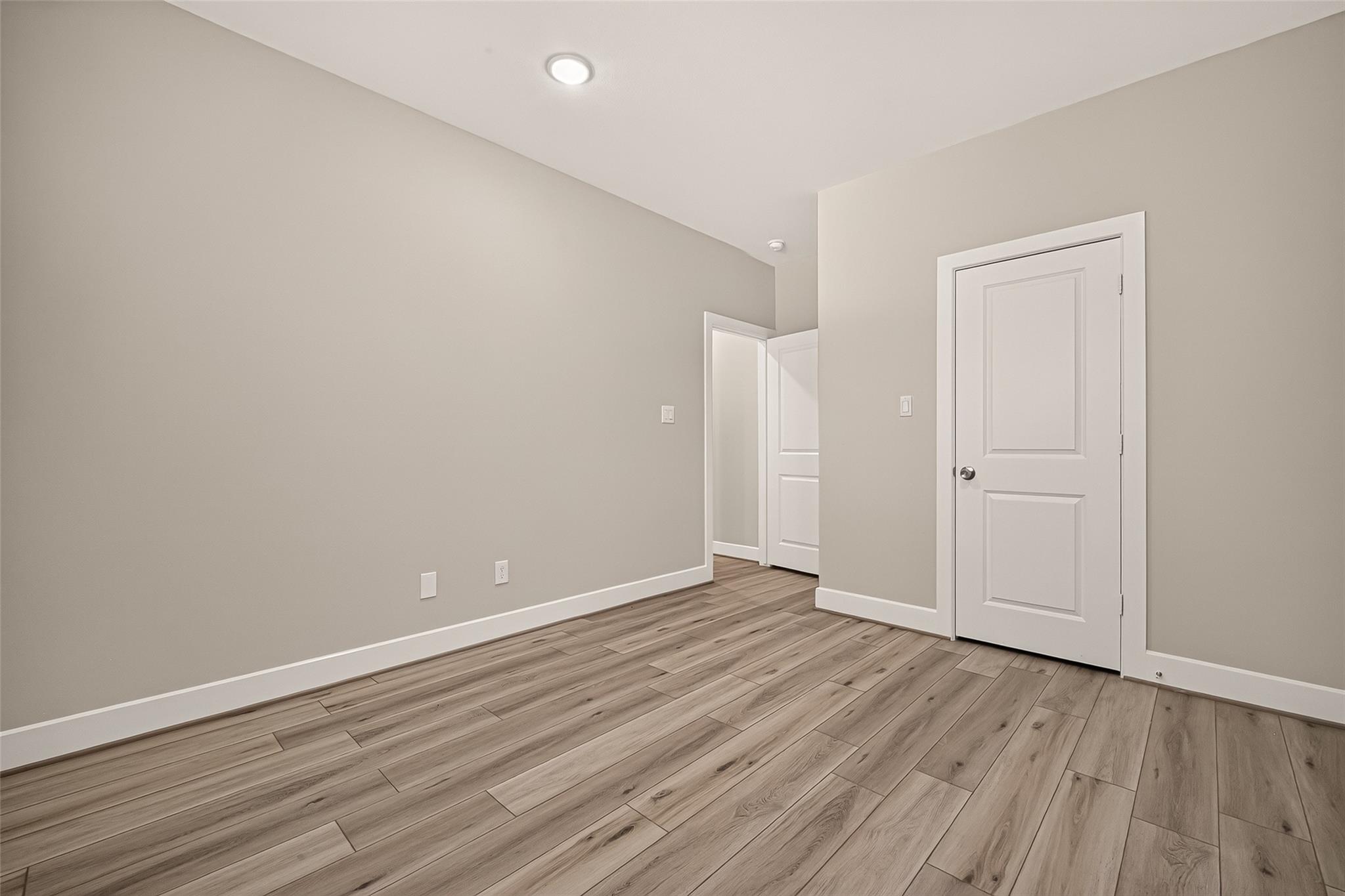 Empty room with wood-look plank flooring, neutral walls, and white paneled doors.
