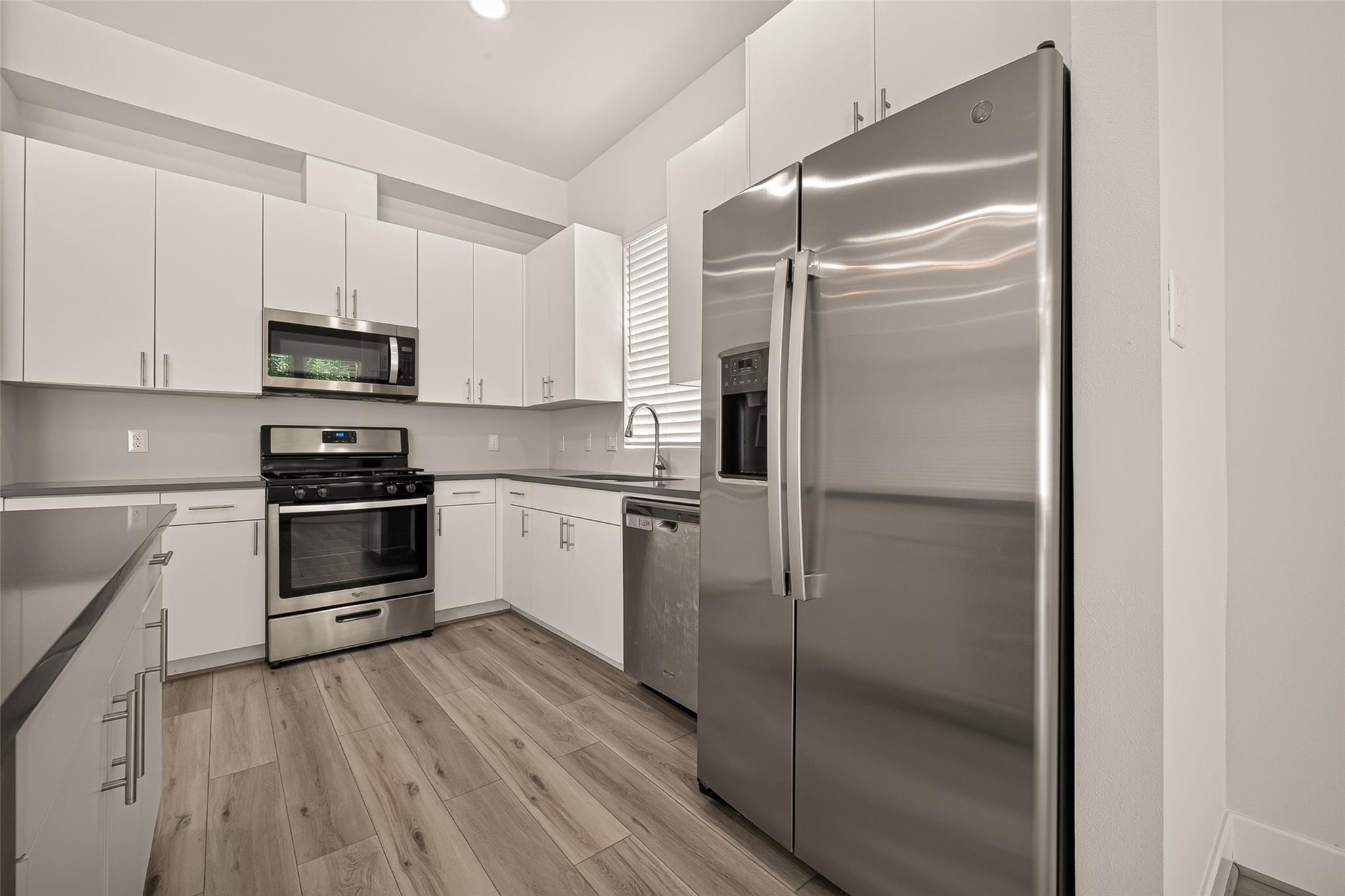 Modern kitchen with white cabinets, stainless steel appliances, and light wood-look flooring.