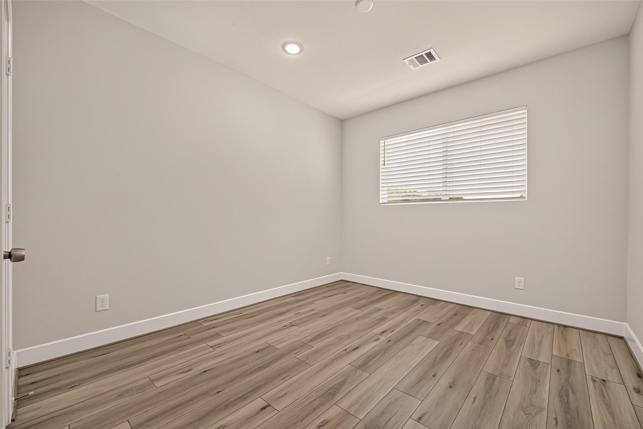 Unfurnished room with wood-look plank flooring and a window with closed blinds.