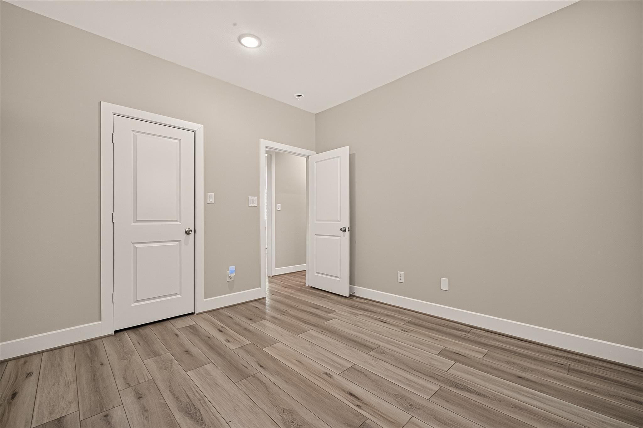 Empty room with taupe walls, white doors, and gray-brown plank flooring.