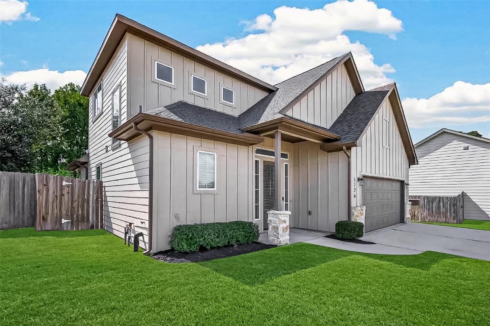 Two-story light-colored home with a covered entry, stone porch columns, and an attached garage.
