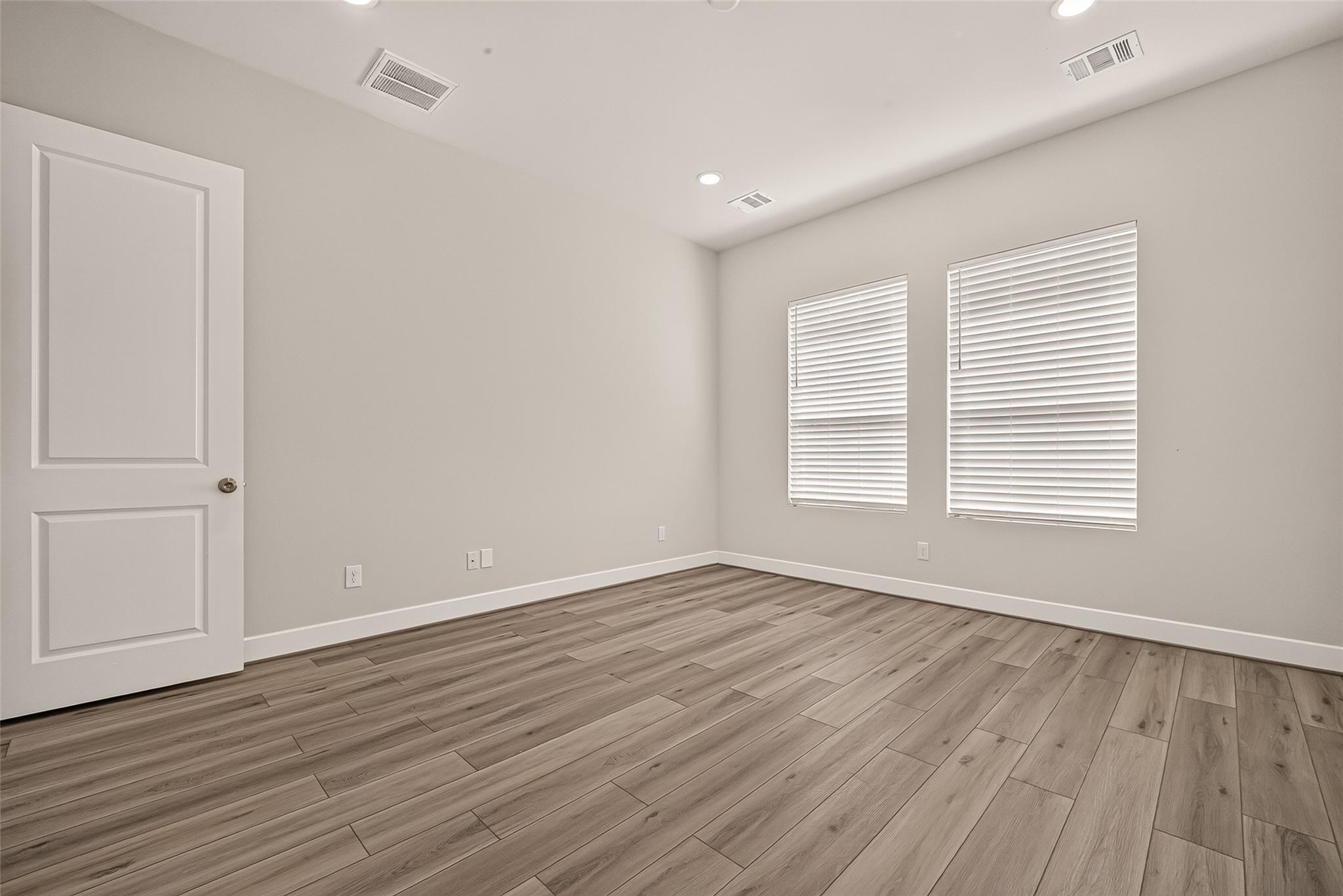 Empty room with wood-look flooring, two windows with white blinds, and an open paneled door.