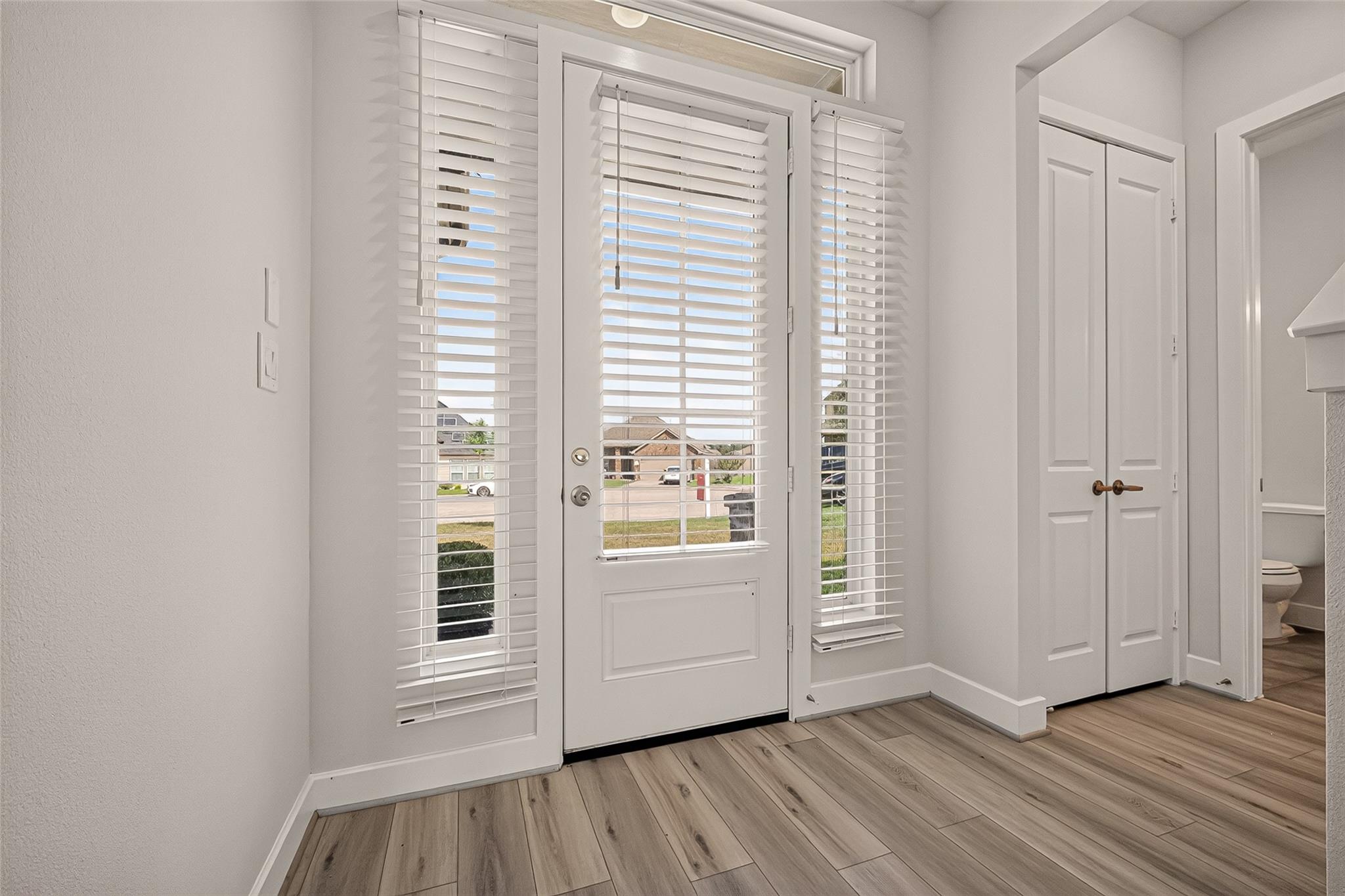 Front entry with a glass-paneled door, white blinds, wood-look flooring, and a double-door closet.
