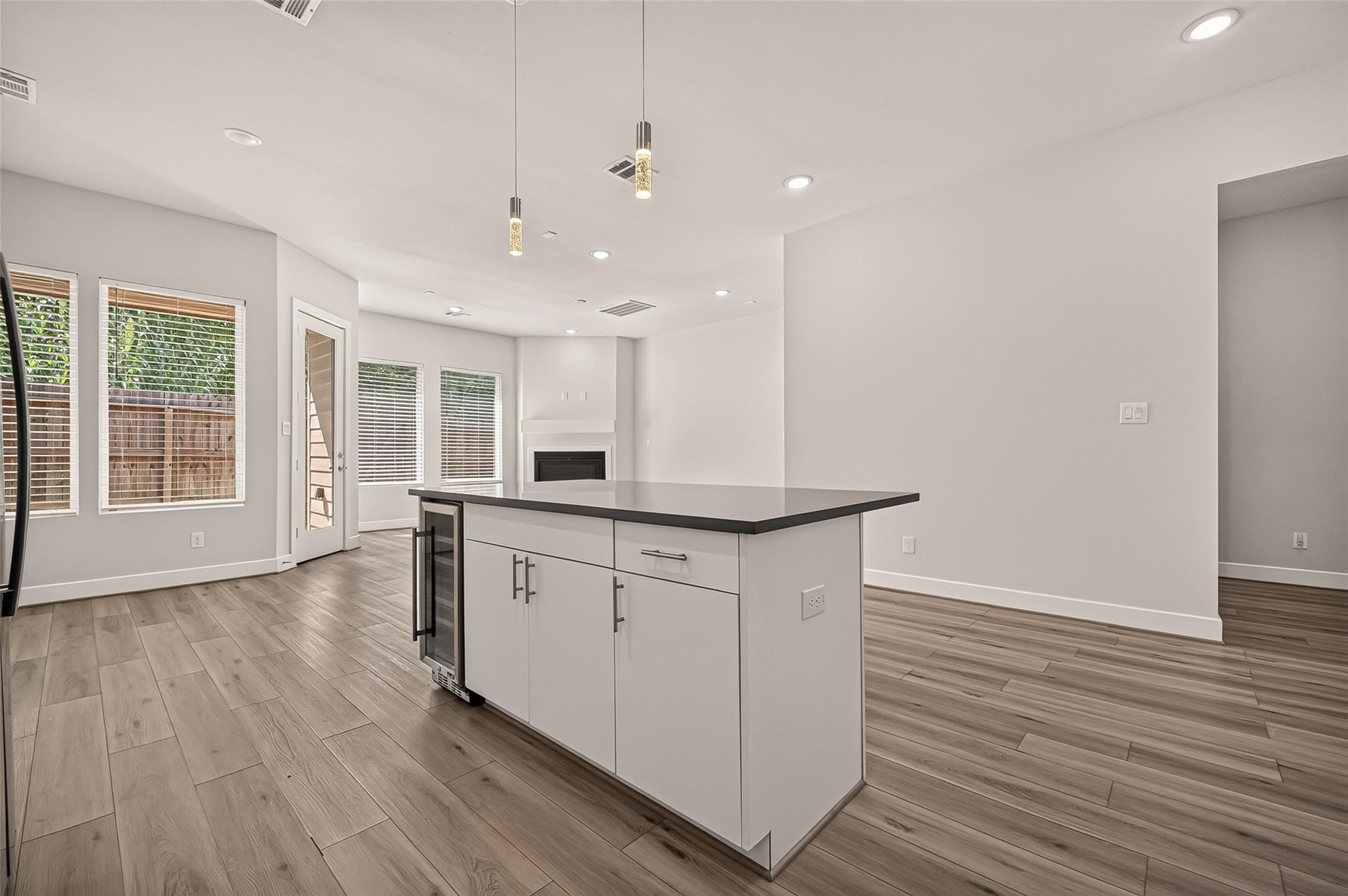 Open-plan kitchen with a large island, wine refrigerator, wood-look floors, and an adjoining fireplace.
