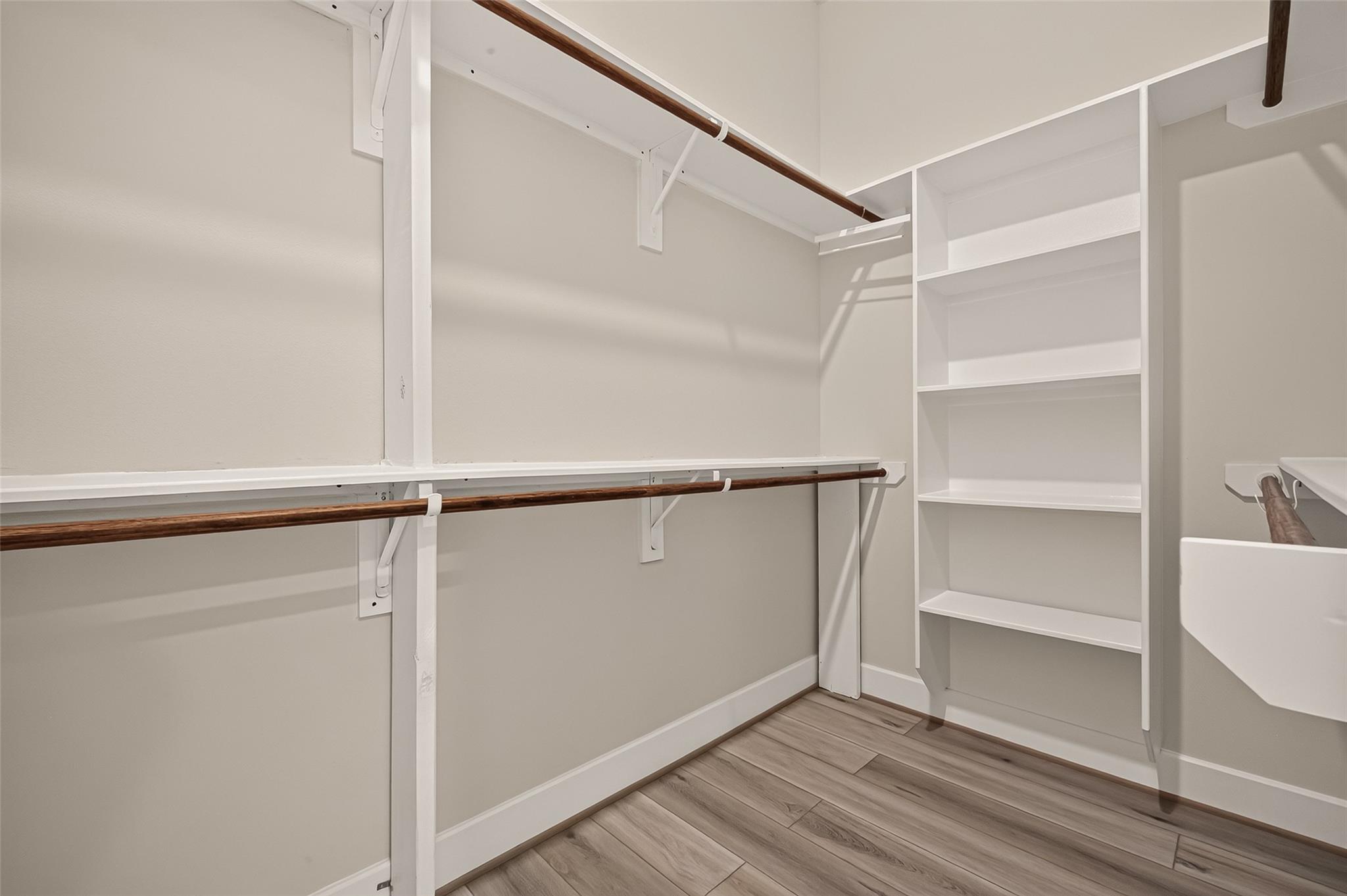 Walk-in closet with built-in white shelving, dark wood hanging rods, and wood-look flooring.