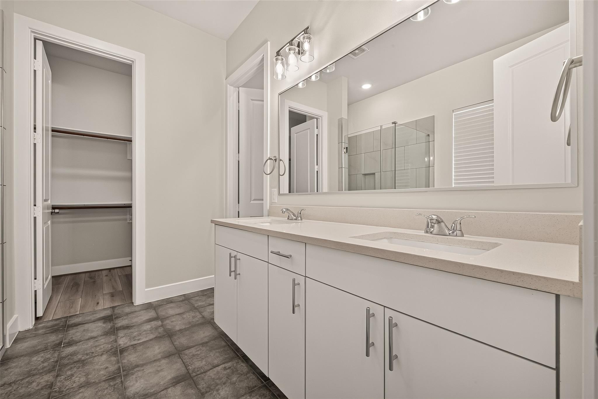 Bathroom with a double vanity, large mirror, glass shower, and open walk-in closet.