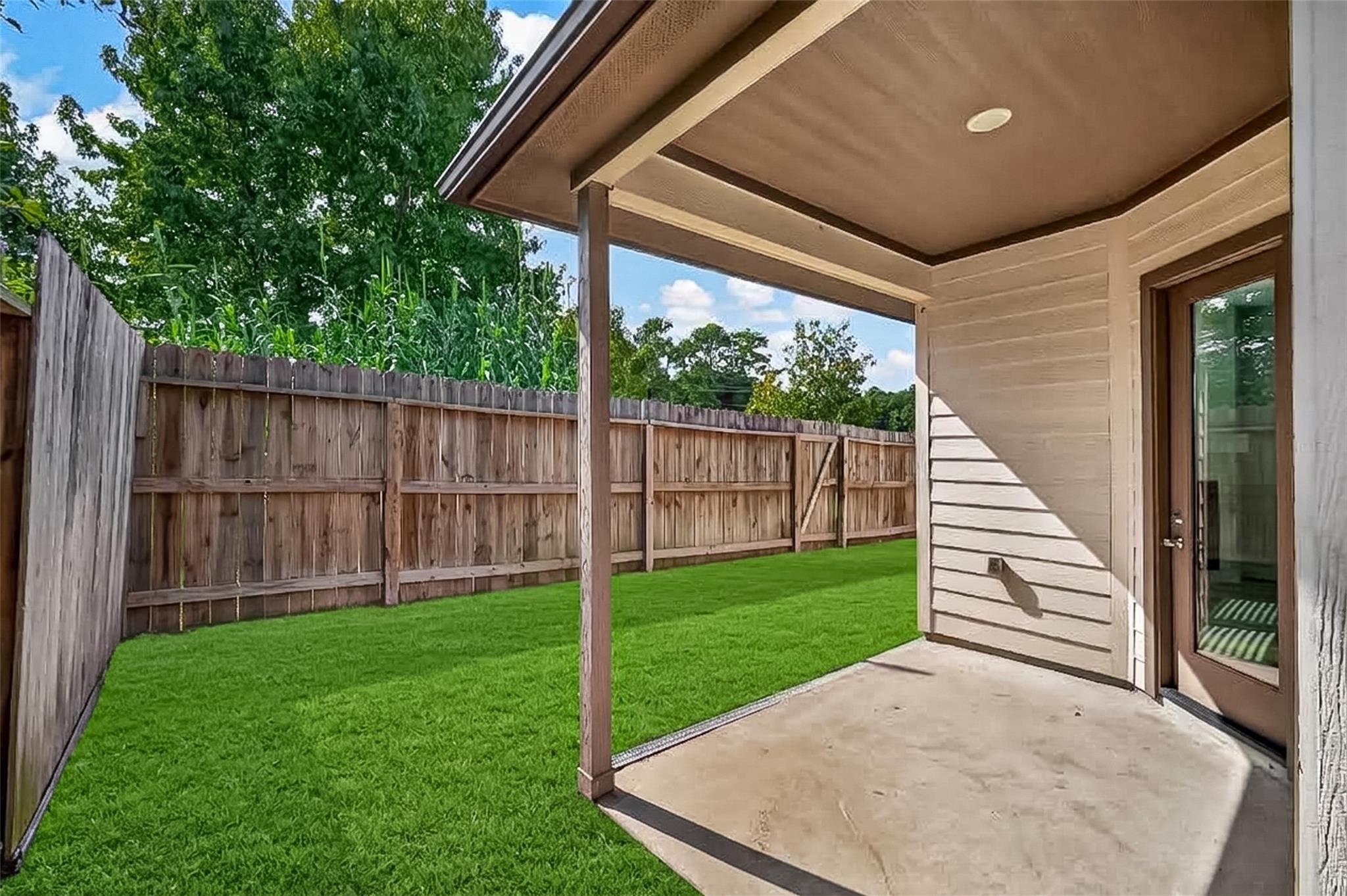 Covered concrete patio beside a neatly mowed, fenced backyard.