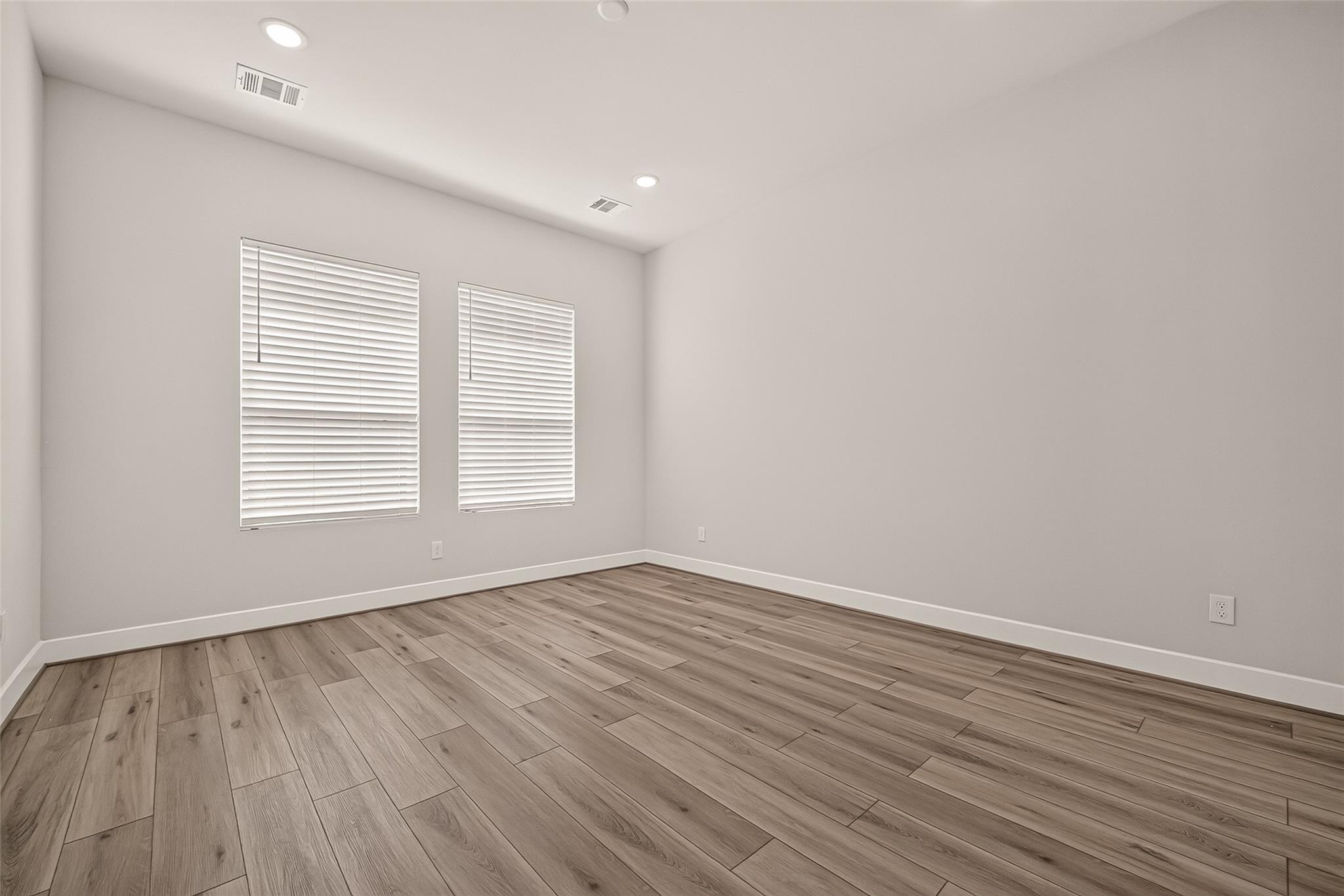 Empty room with two windows, white blinds, and wood-look plank flooring.