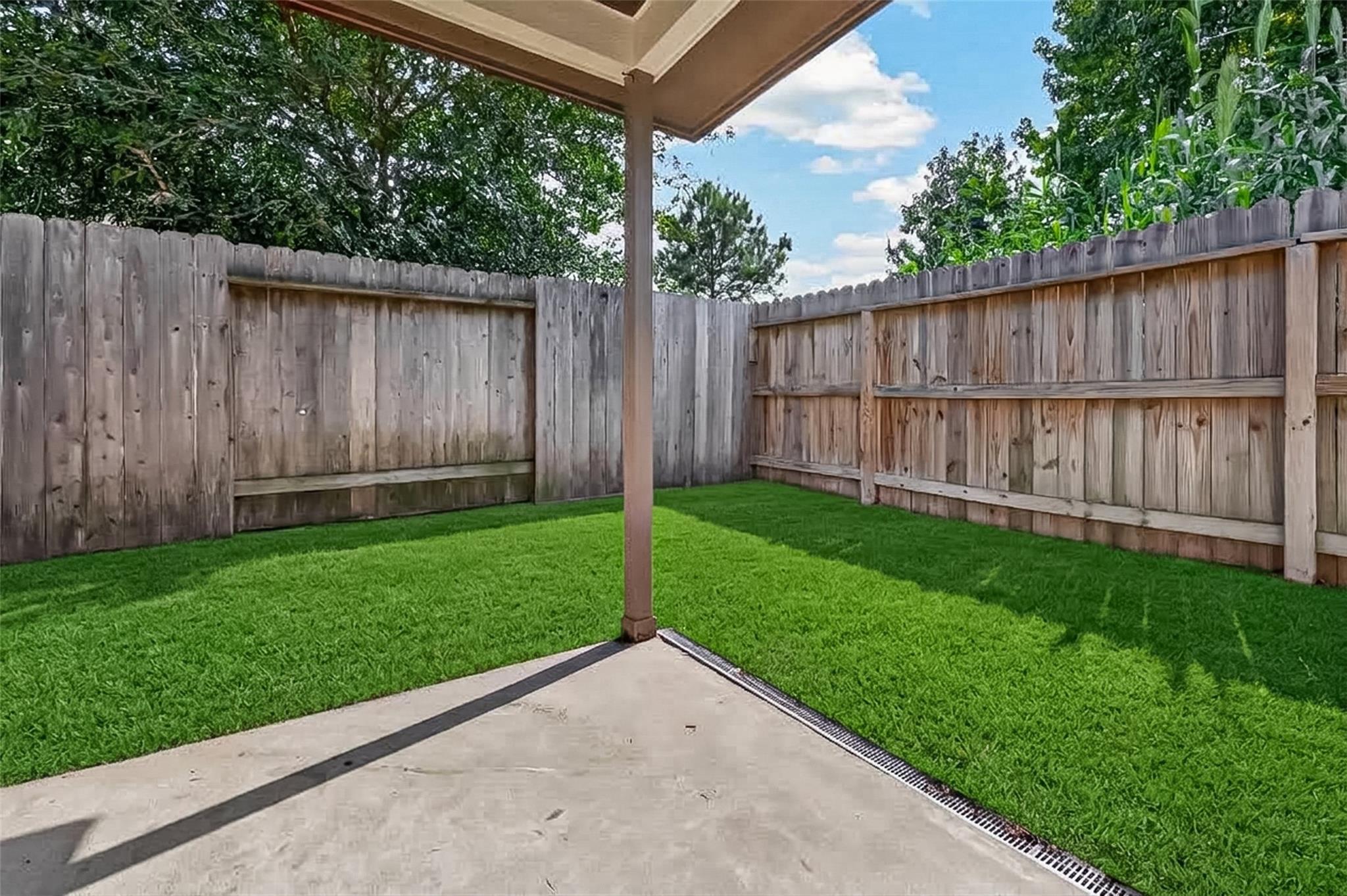 Fenced backyard with a covered concrete patio and neatly maintained green lawn.