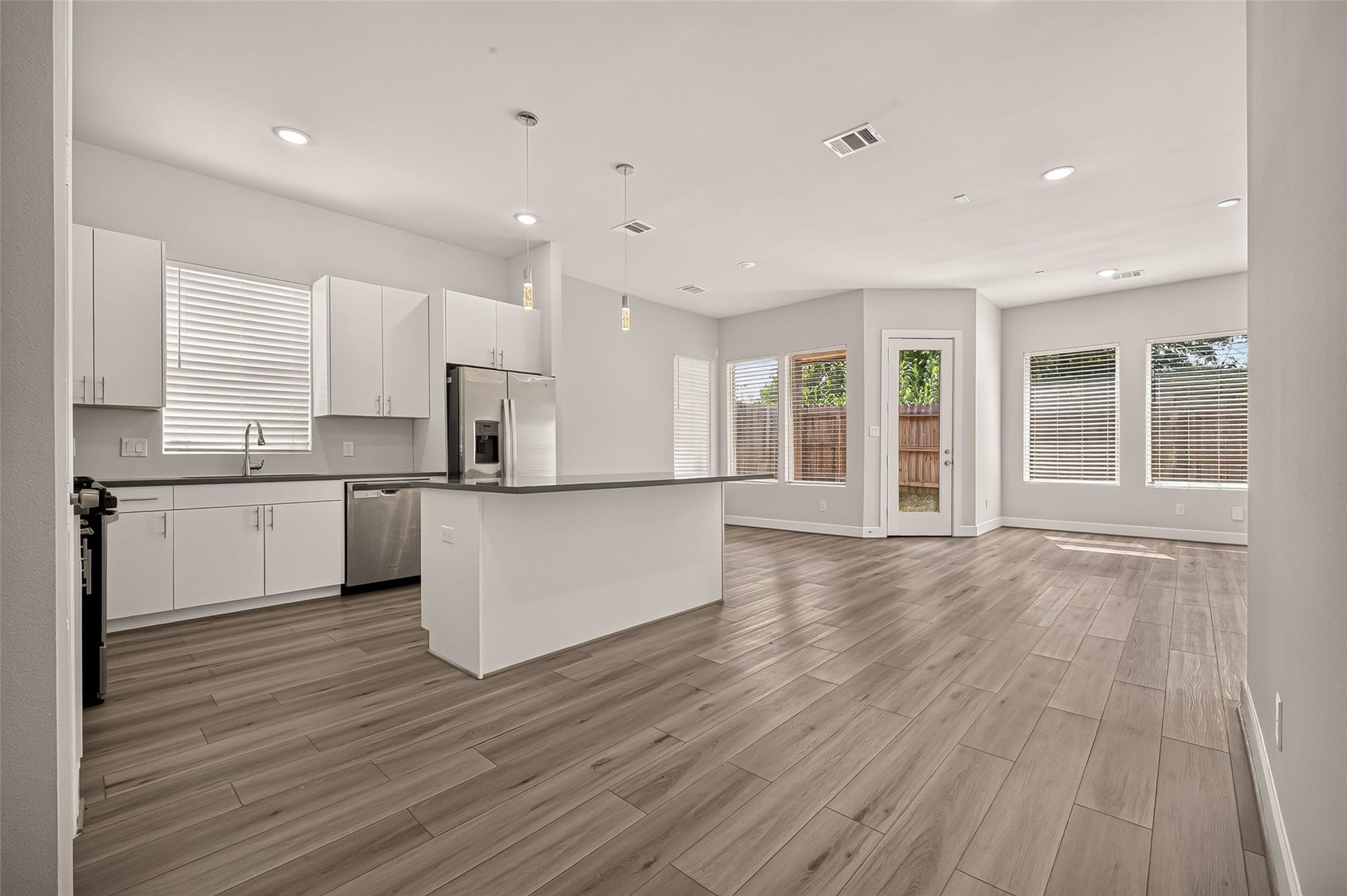 Open kitchen and living area with a white island, stainless appliances, and wood-look tile floors.