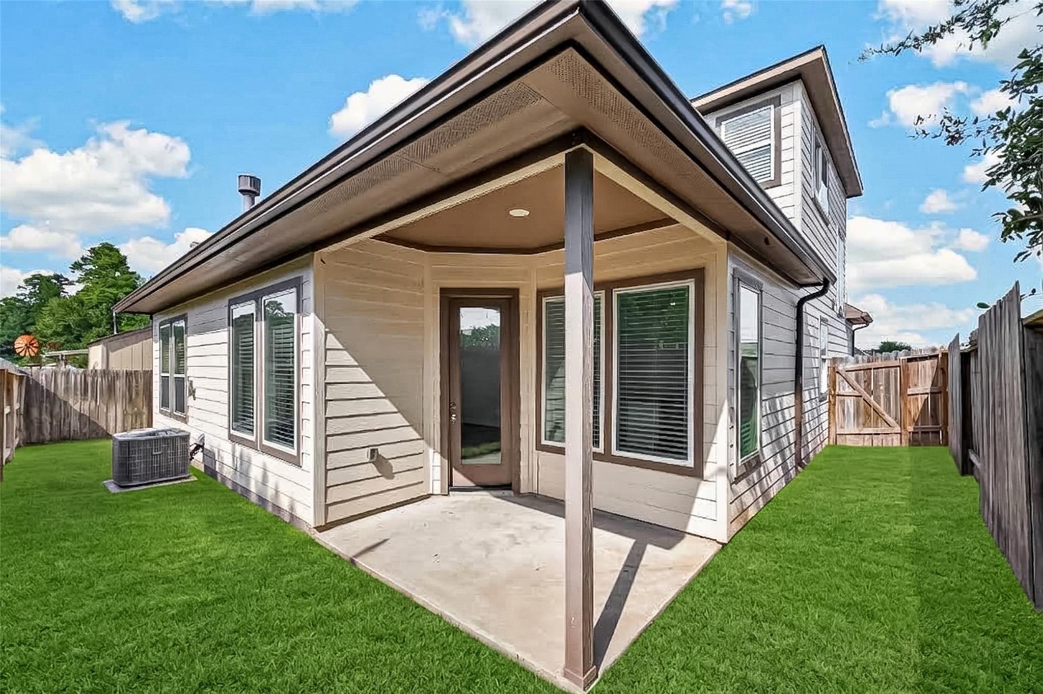 Home’s rear exterior with a covered patio, fenced backyard, and green lawn.