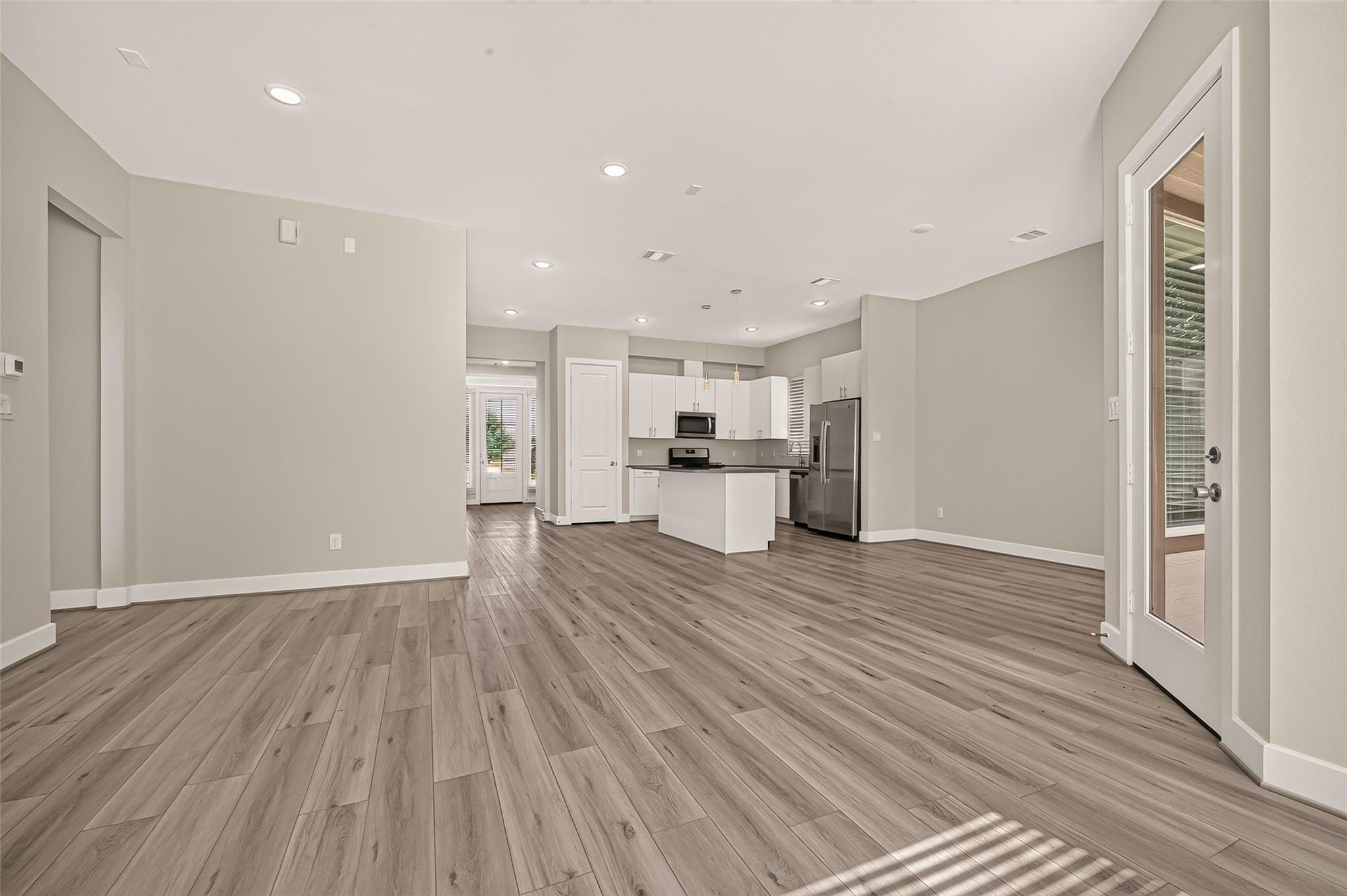 Empty open-plan living area with wood-look floors, a white kitchen island, and stainless steel appliances.