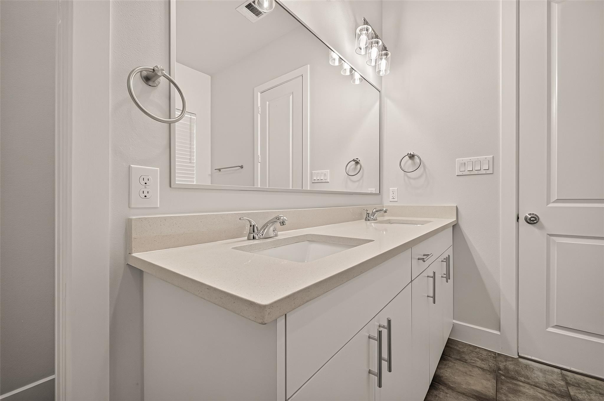 Bathroom with a long white double-sink vanity, large mirror, and dark tile floor.