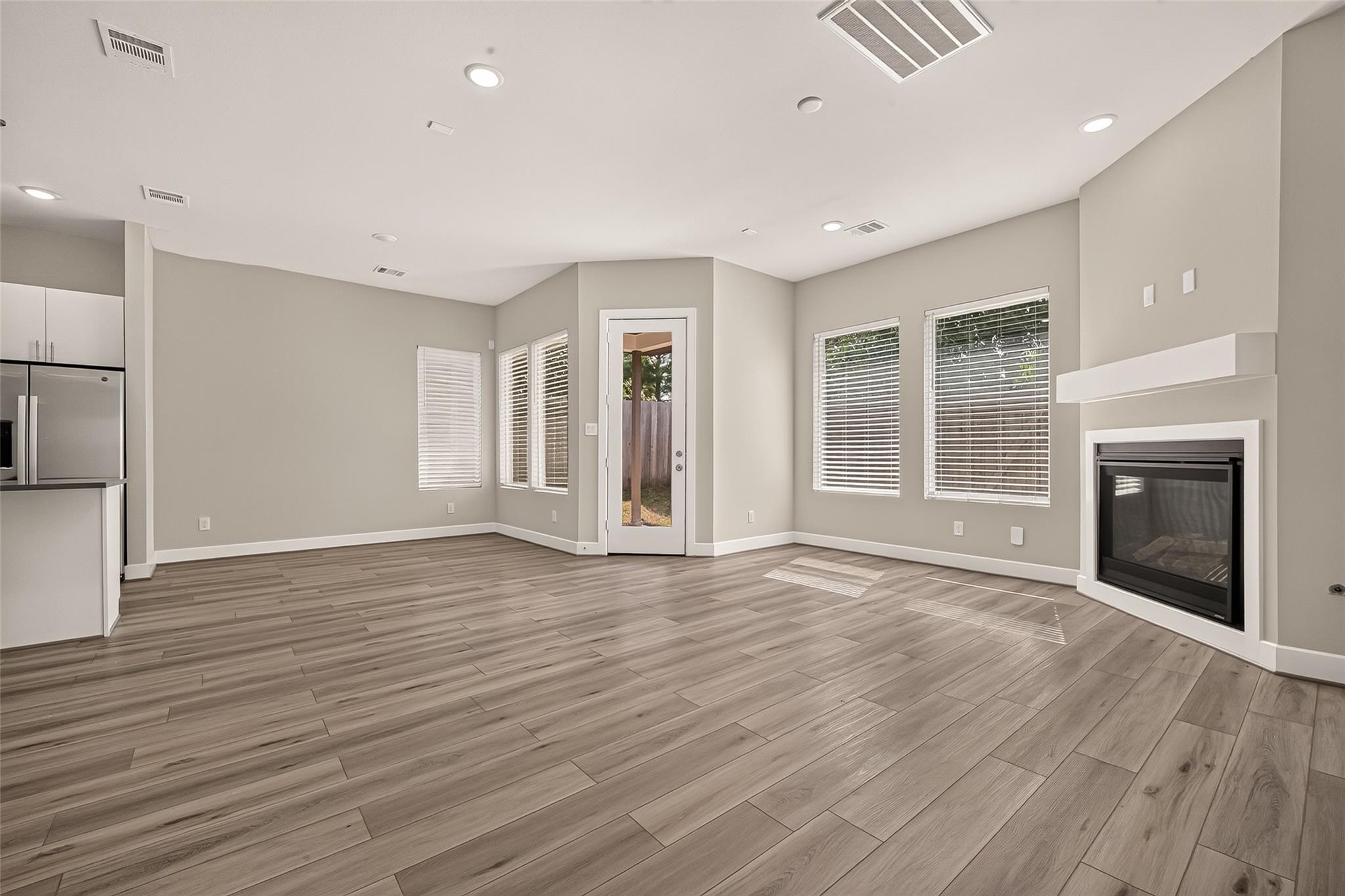Empty living room with wood-look floors, window blinds, glass back door, and built-in fireplace.