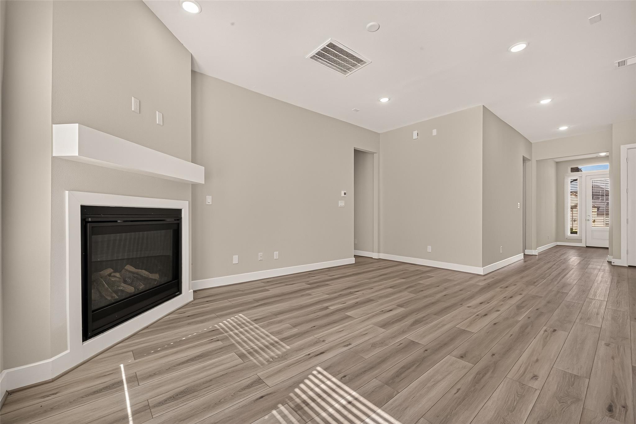 Vacant living room with a gas fireplace, wood-look flooring, and shuttered glass doors at the back.