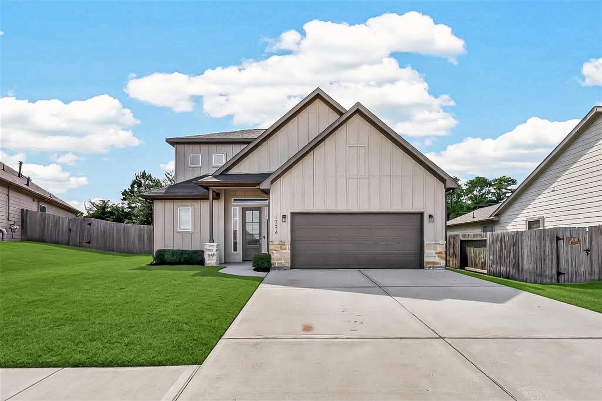 Two-story beige home with prominent gables, double garage, wide driveway, and green front lawn.