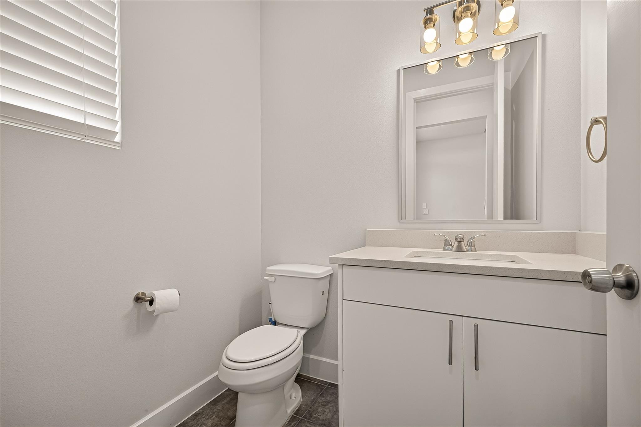 Bathroom with a white vanity, large mirror, toilet, and window blinds.