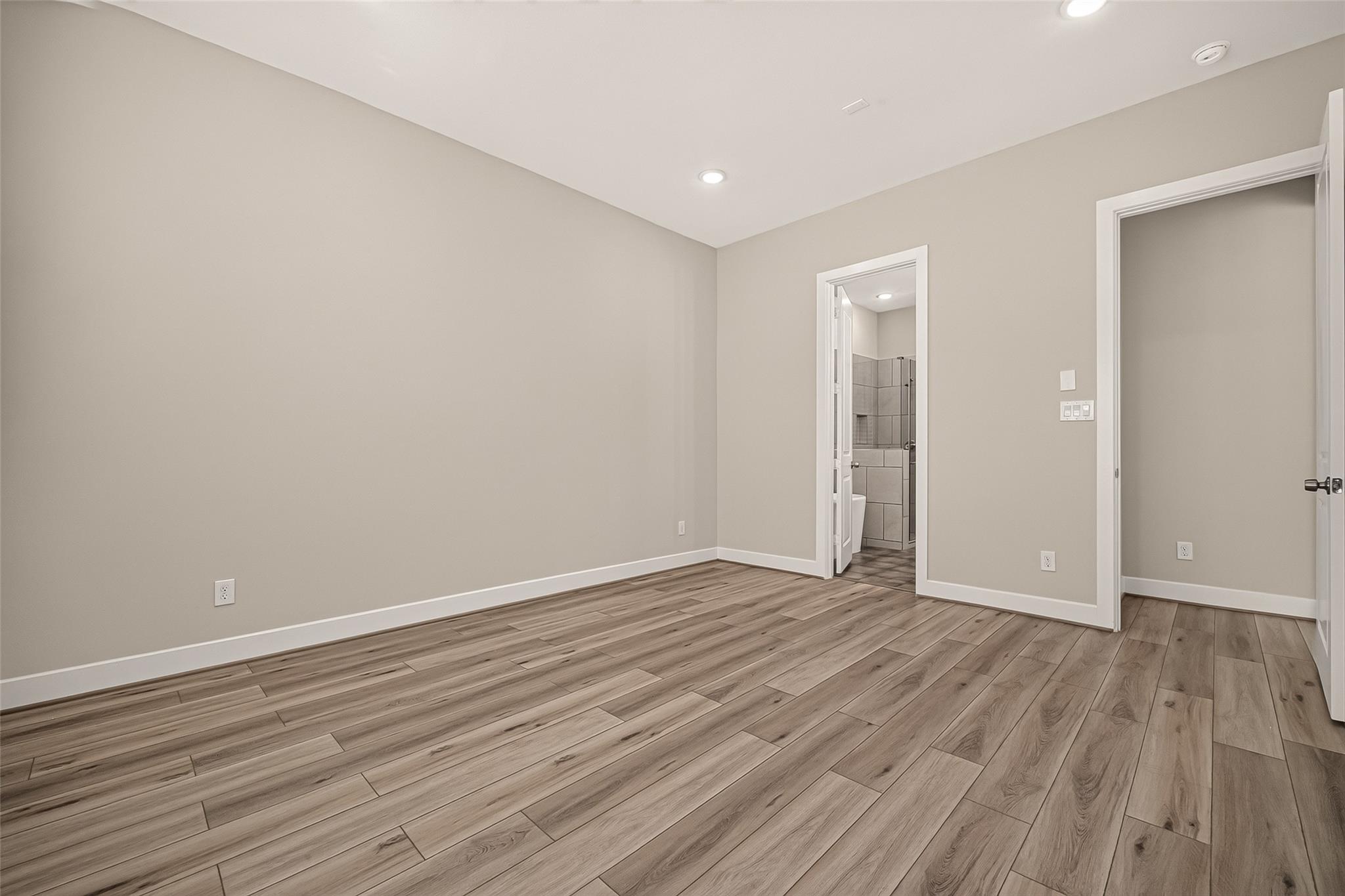 Empty bedroom with wood-look plank flooring and an open doorway to a tiled bathroom.