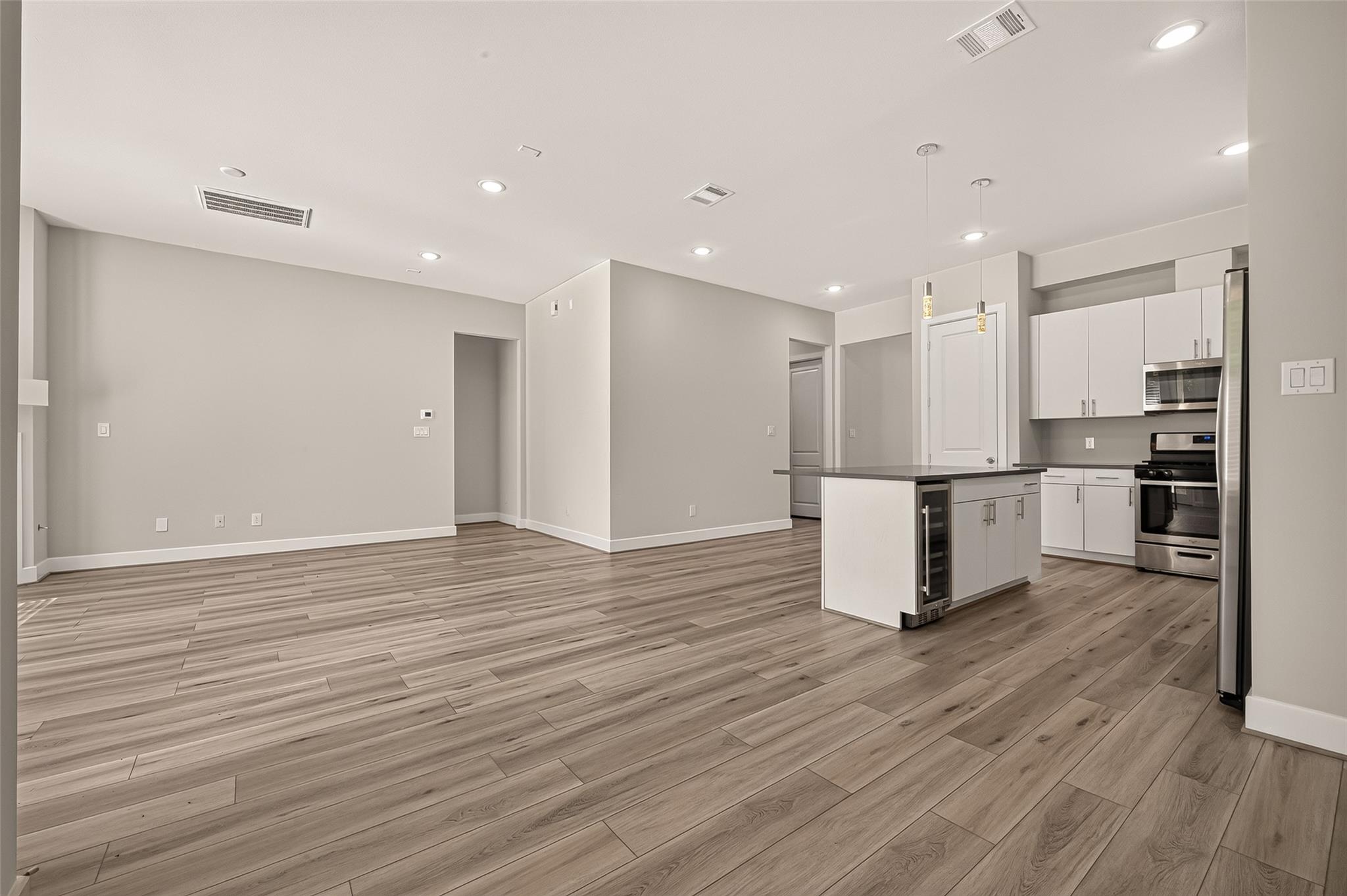Empty open-plan kitchen with white cabinets, stainless steel appliances, and a dark-topped island.