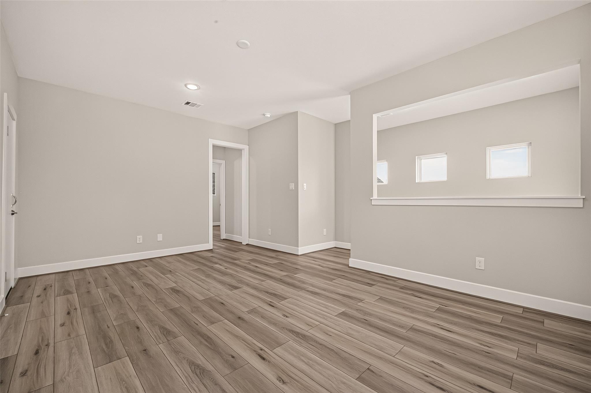 Empty room with wood-look plank flooring and a wide pass-through opening with three windows.