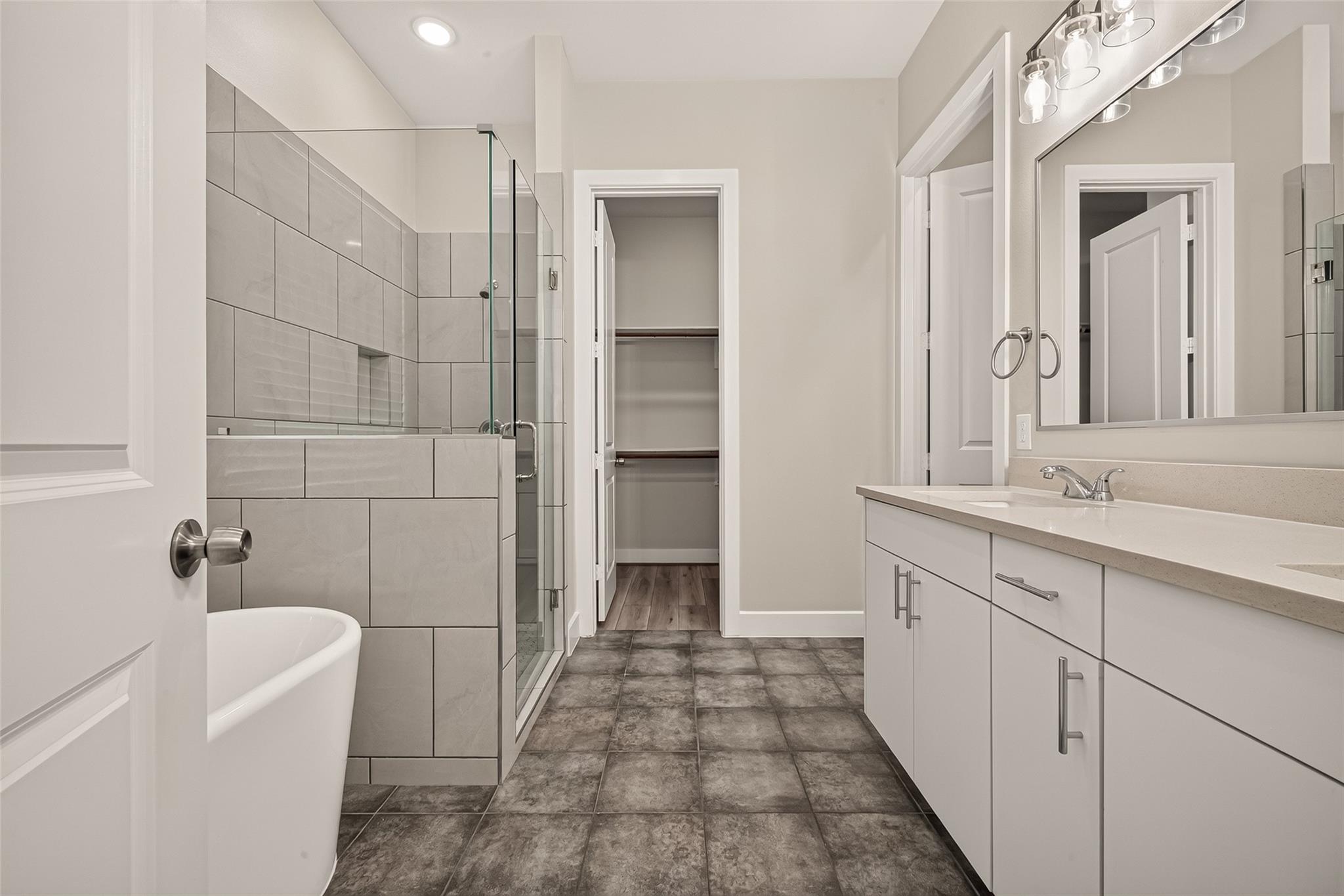 Bathroom with a glass shower, freestanding tub, white vanity, and open walk-in closet.