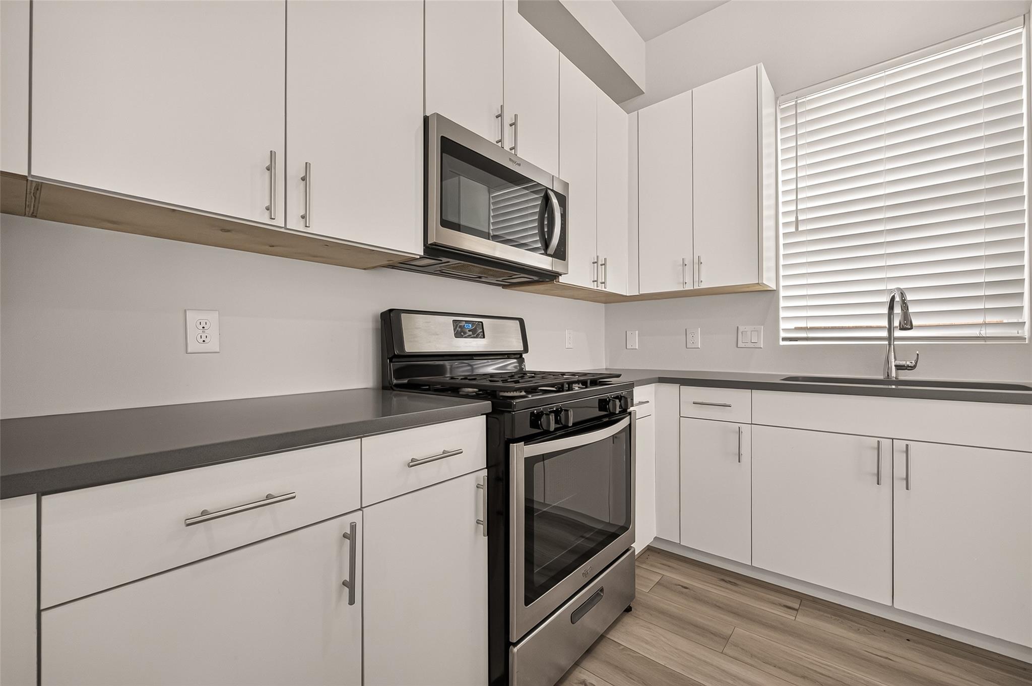 Modern kitchen with white cabinets, dark countertops, stainless steel appliances, and a sink beneath a window.