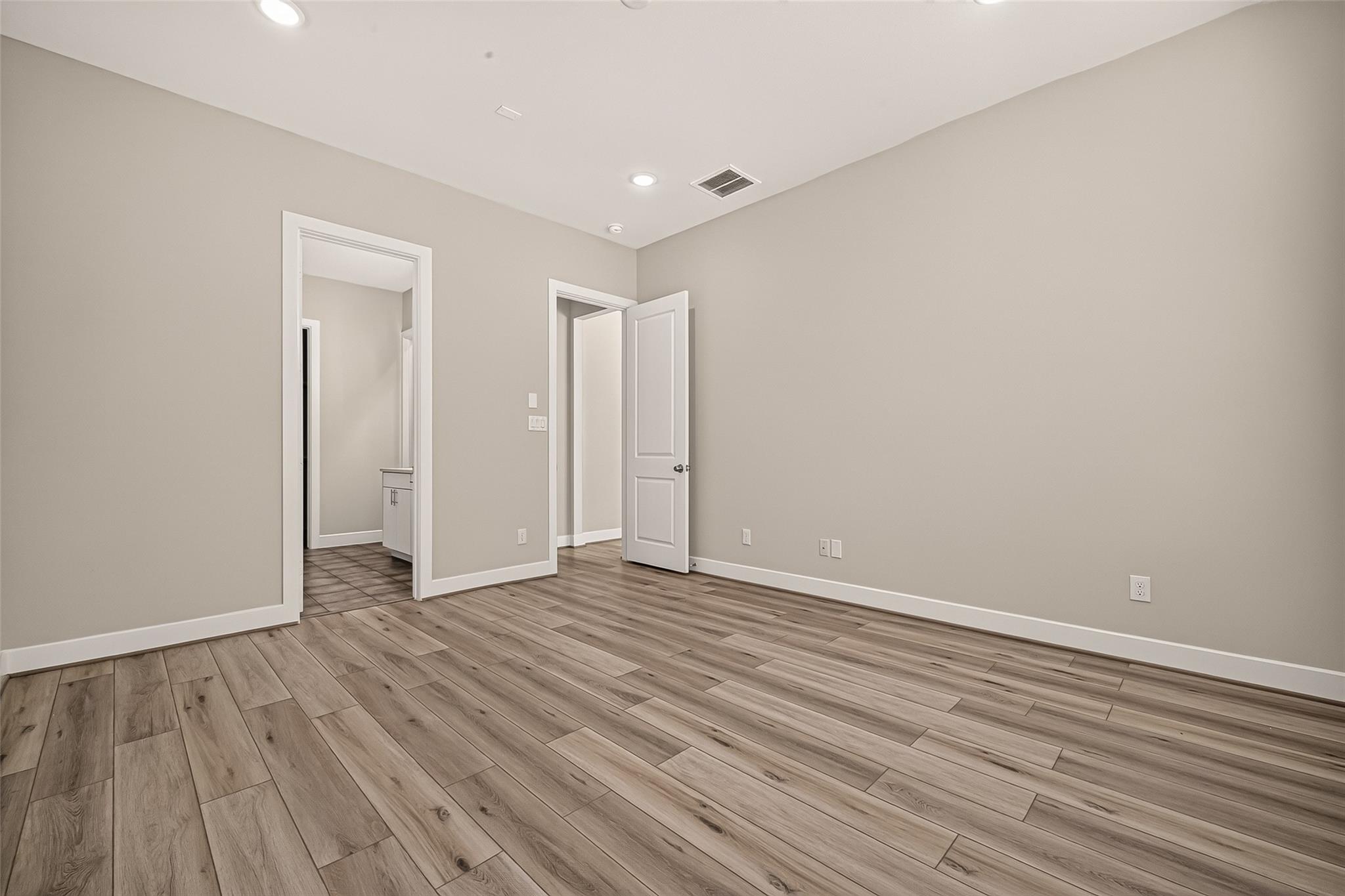 Empty room with wood-look flooring, recessed lights, and open doorways.