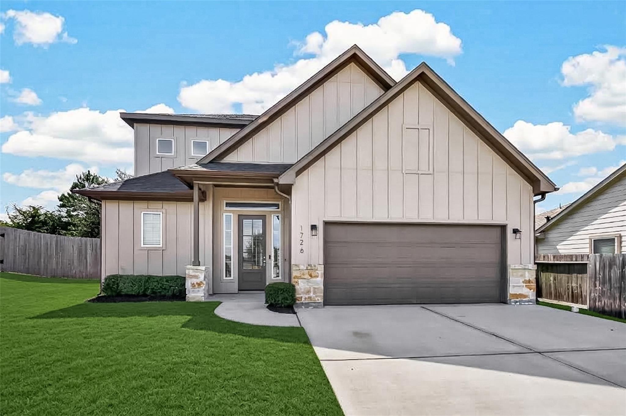 Two-story house with prominent gables, a double garage, stone accents, and a green front lawn.