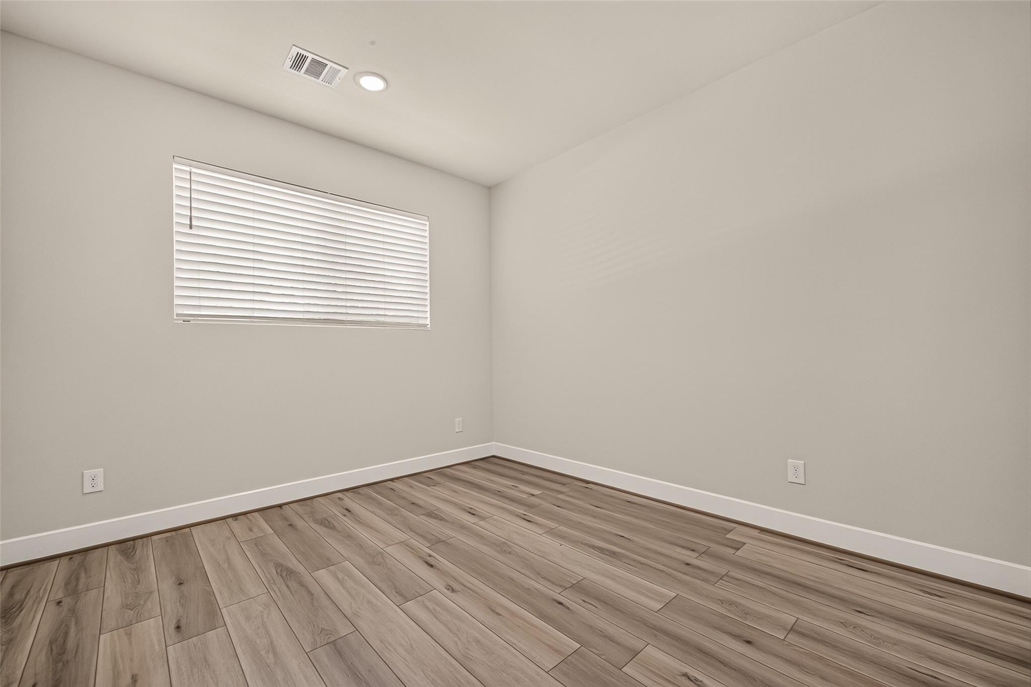 Empty room with closed window blinds and wood-look plank flooring.