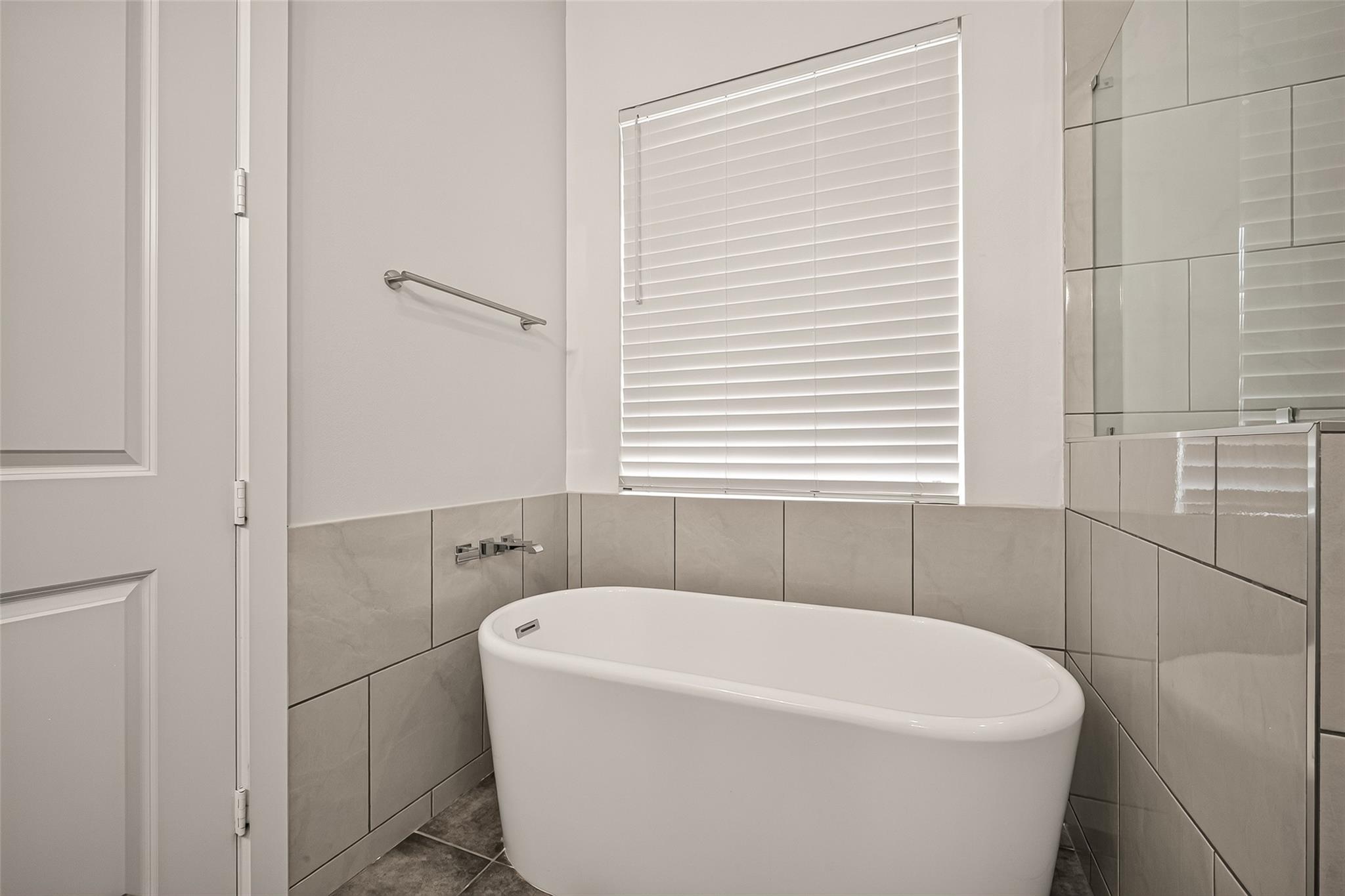 Modern bathroom with a white freestanding soaking tub beneath a window with closed blinds.