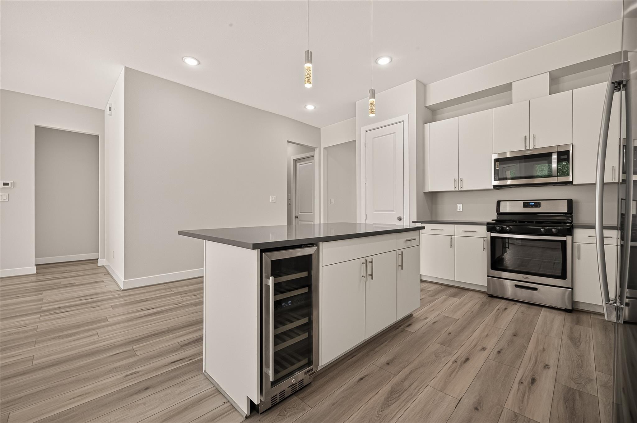 Modern kitchen with a large island, built-in wine refrigerator, white cabinets, and stainless steel appliances.
