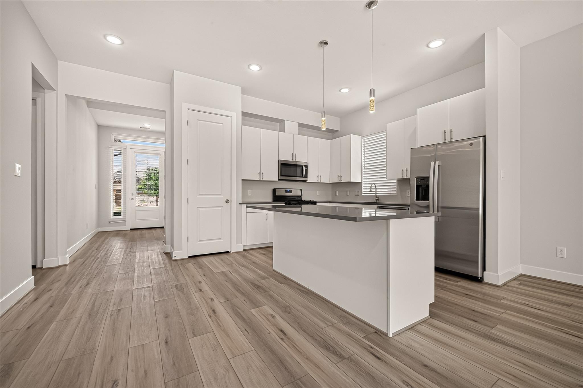 Vacant kitchen with a large island, white cabinets, stainless steel appliances, and wood-look flooring.