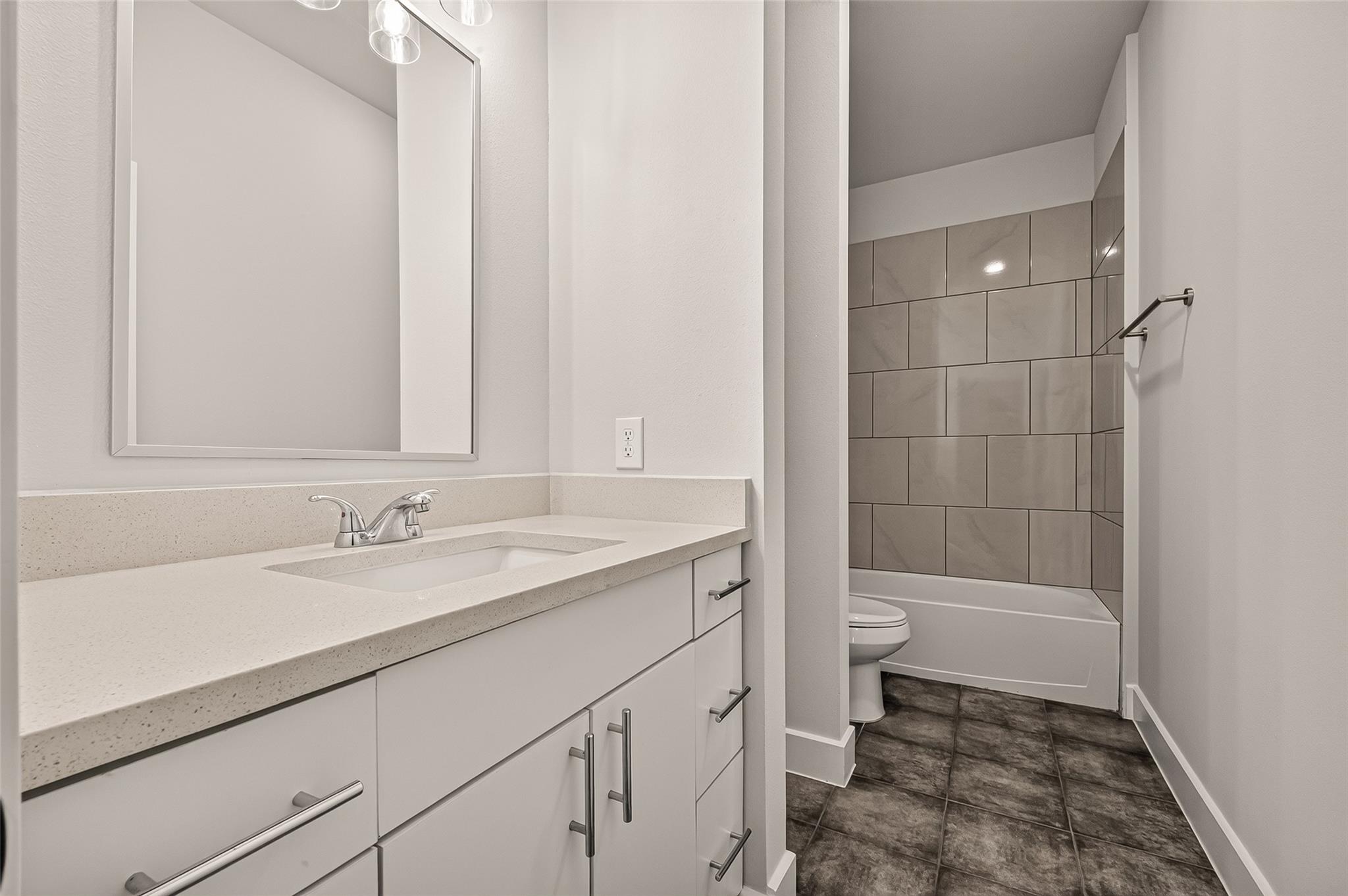 Bathroom with a long white vanity and mirror beside a gray-tiled tub-shower.