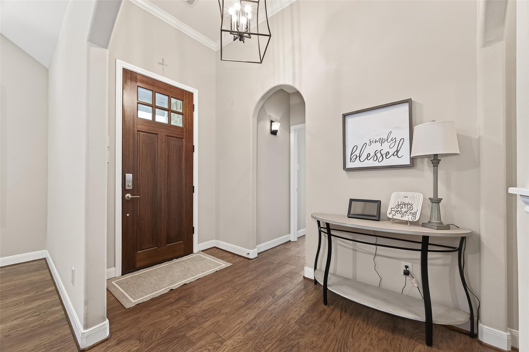 Entry foyer with a dark wood, glass-paneled front door and console table beneath a “simply blessed” sign.