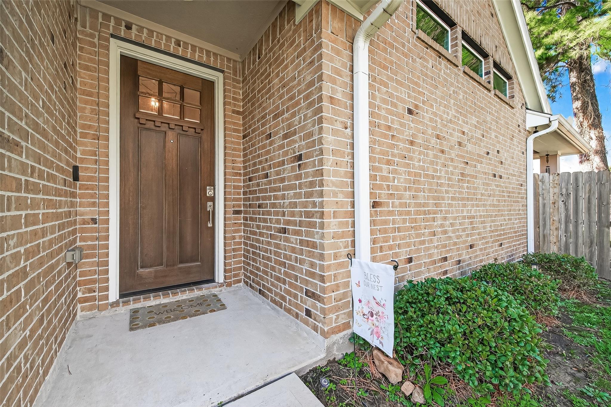 Brick home entry with a dark wood door, covered porch, and trimmed shrubs.