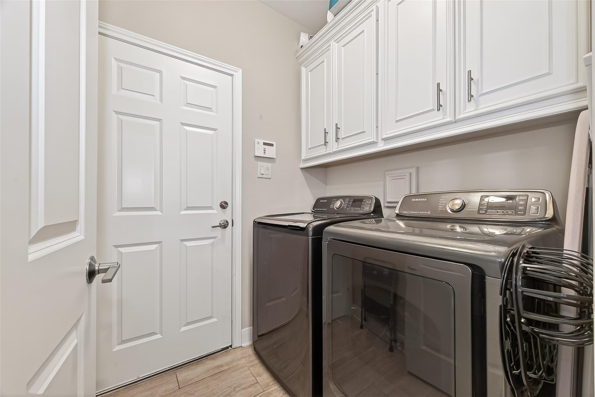 Laundry room with matching dark Samsung washer and dryer beneath white cabinets.