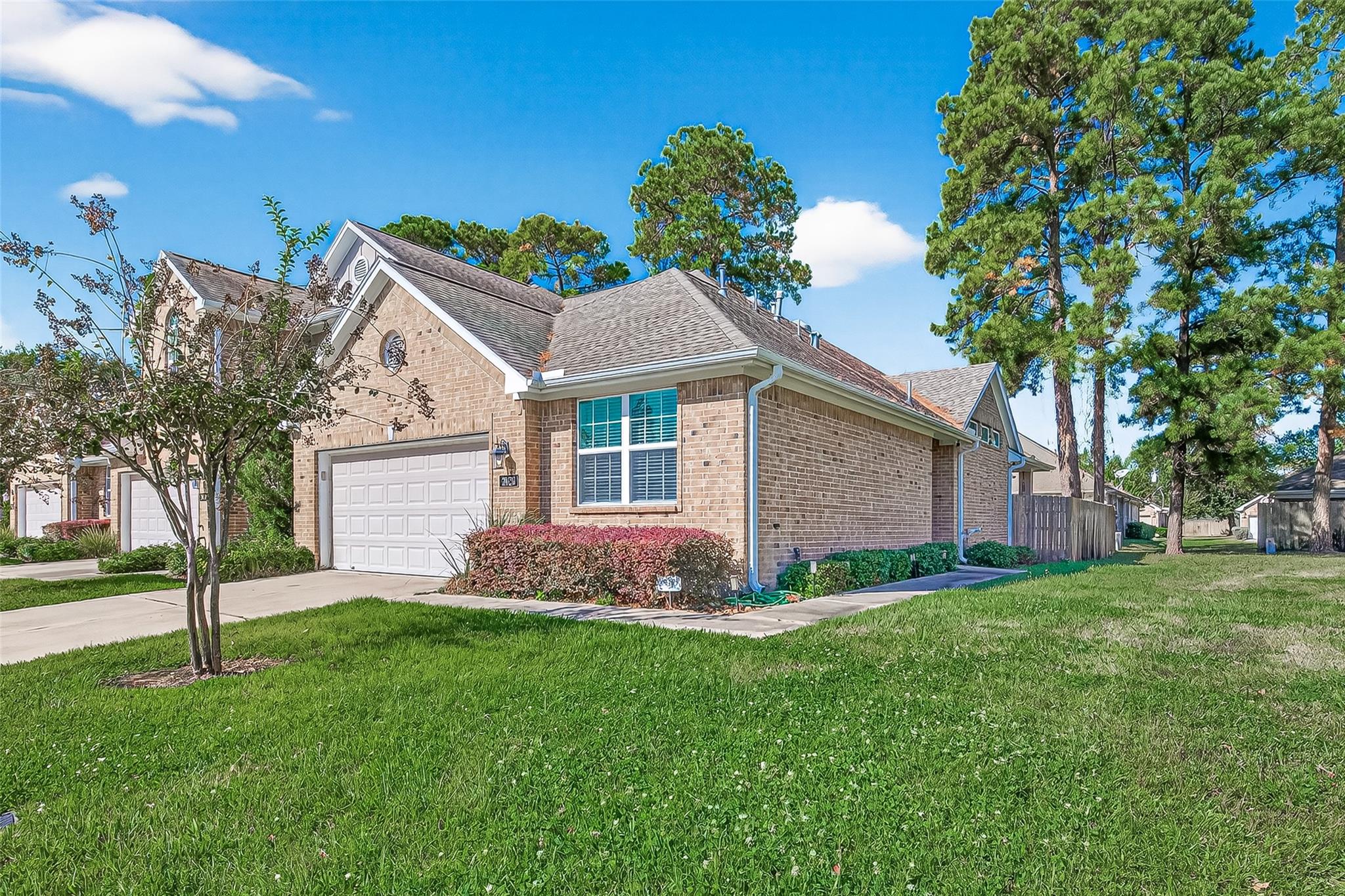 One-story brick home with a white double garage door, front lawn, and mature trees.