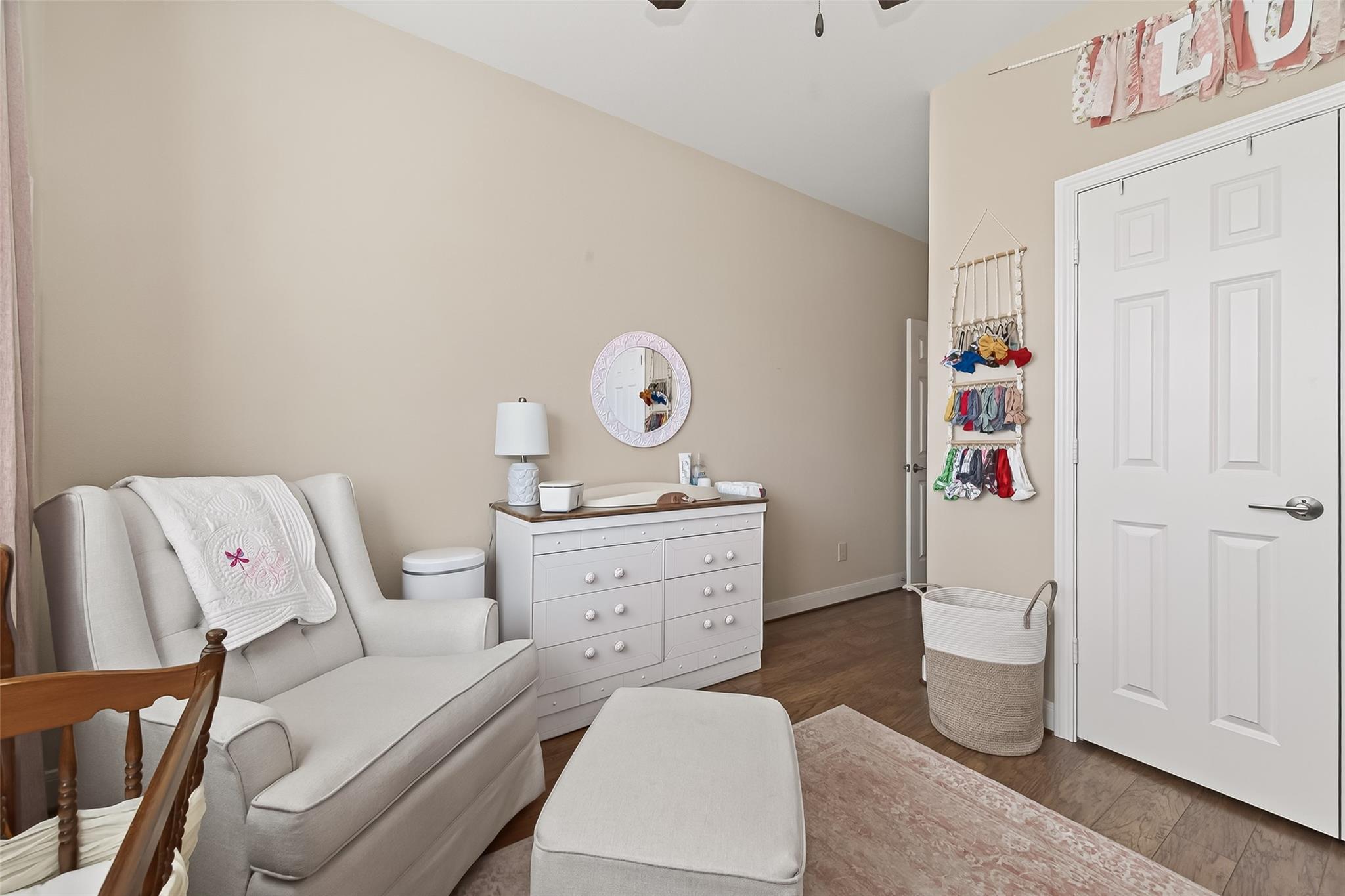 Nursery with a white glider and ottoman, dresser, changing pad, and baby clothes organizer.