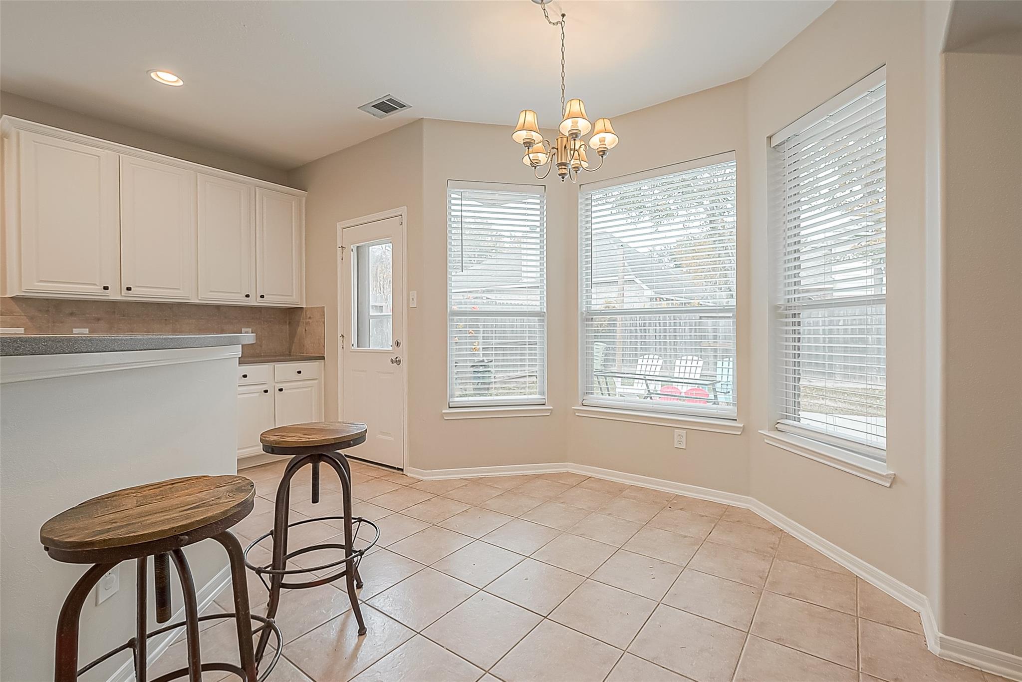 Breakfast area with tiled floors, a breakfast bar, chandelier, and three large windows.