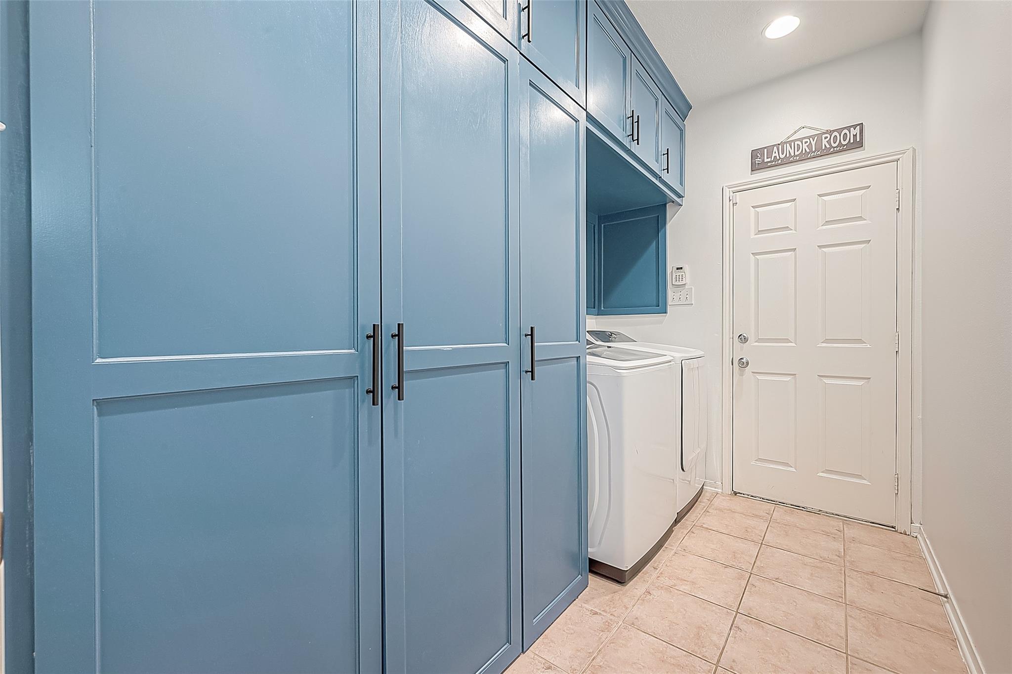 Laundry room with blue built-in cabinets, washer and dryer, and beige tile flooring.