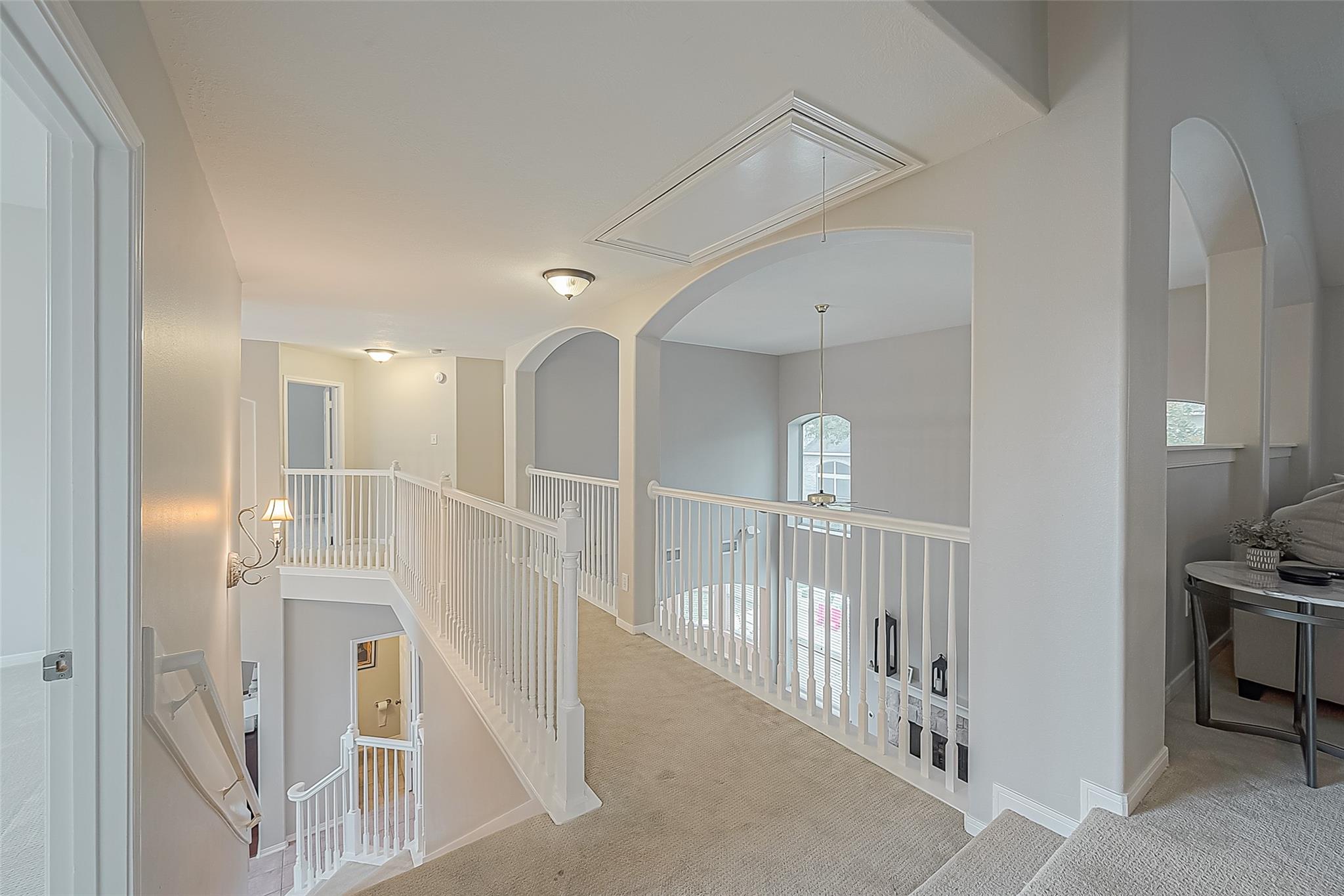 Upstairs landing overlooking the lower floor, with white railings, arched openings, and a carpeted staircase.