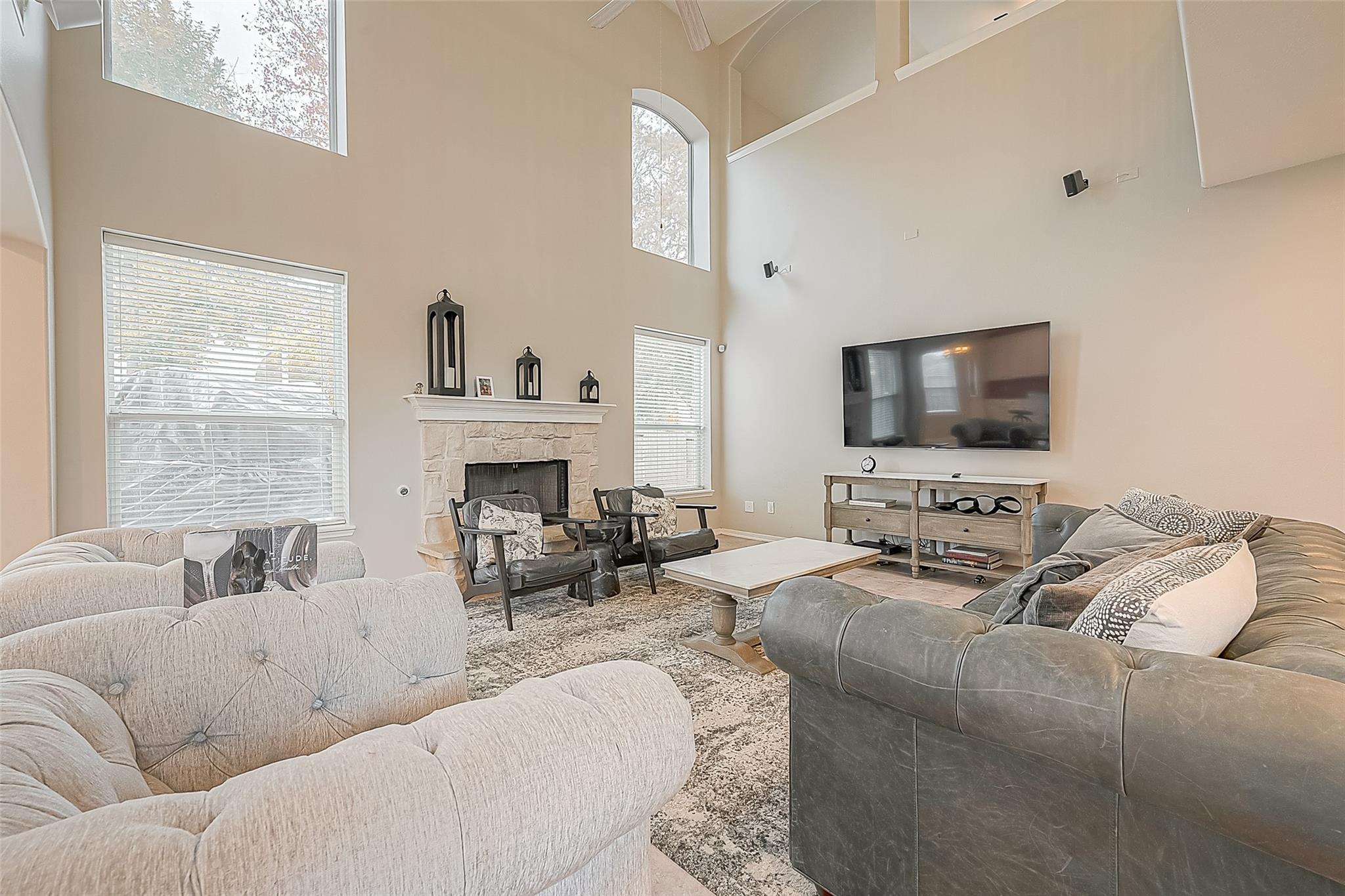 Furnished living room with a stone fireplace, high ceilings, and tall windows.