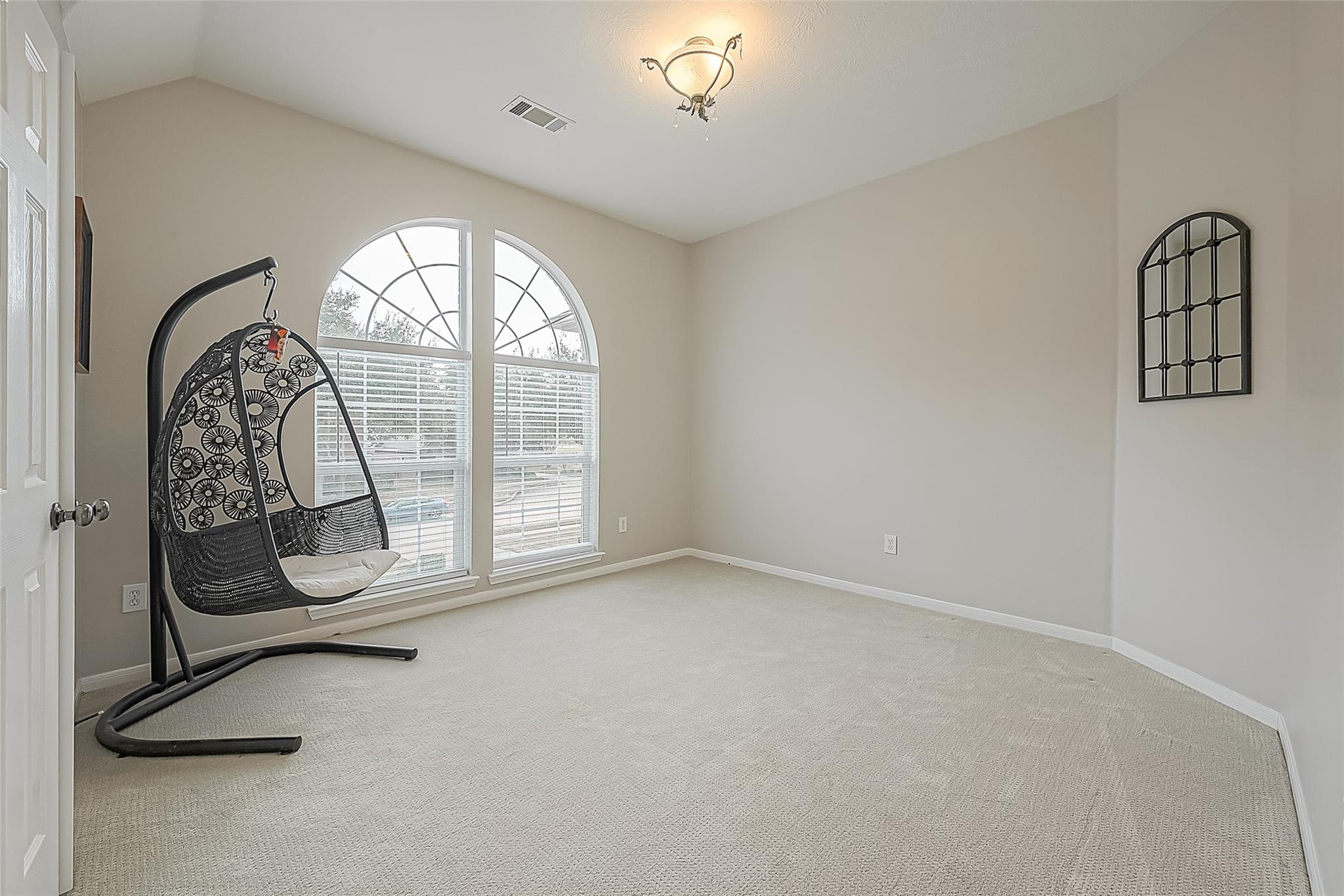 Carpeted bedroom with arched windows and a black hanging egg chair.