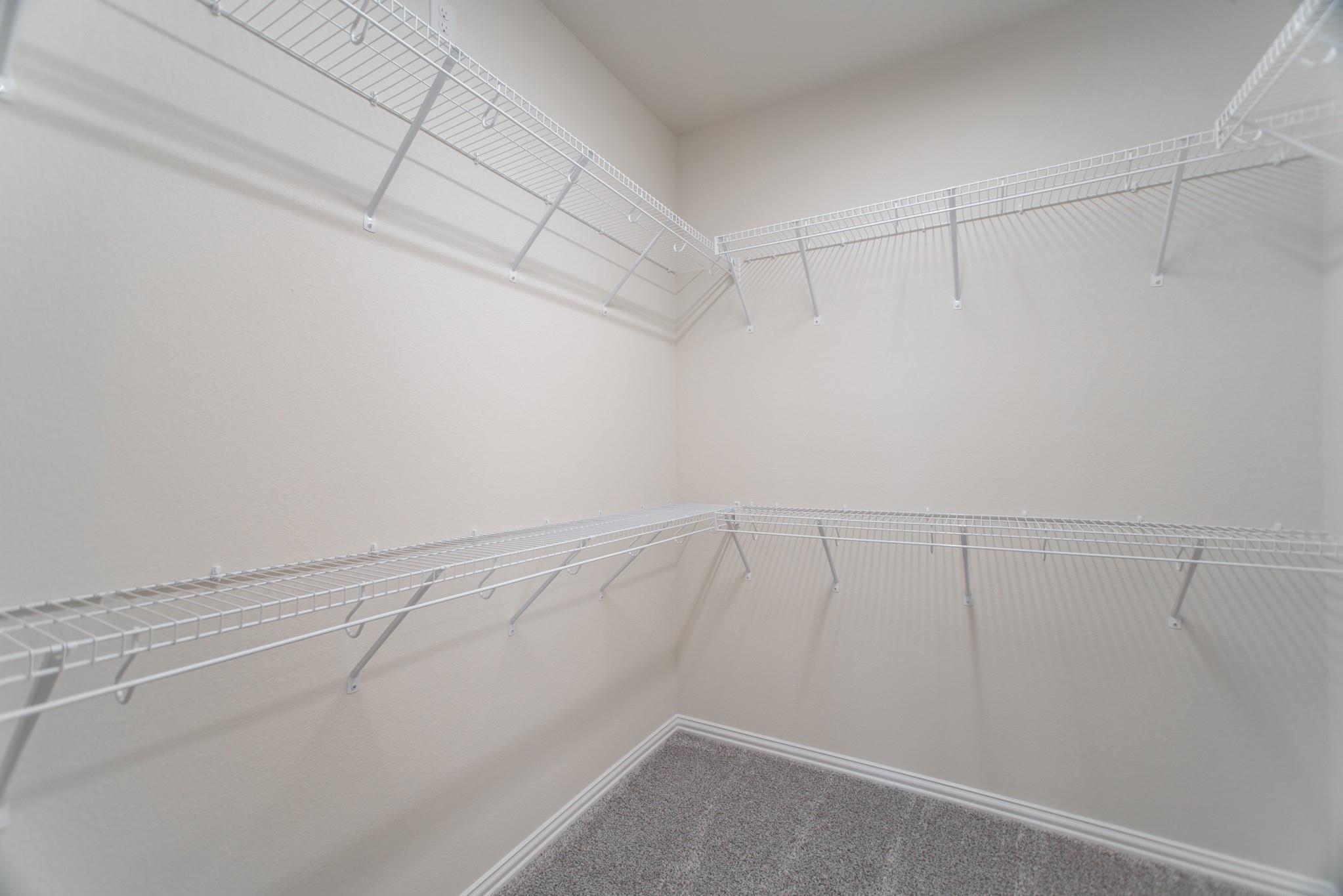 Empty walk-in closet with wraparound white wire shelving and gray carpet.