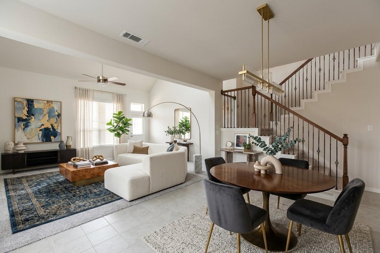 Open-plan living and dining room with white seating, a blue patterned rug, and a staircase with dark railings.