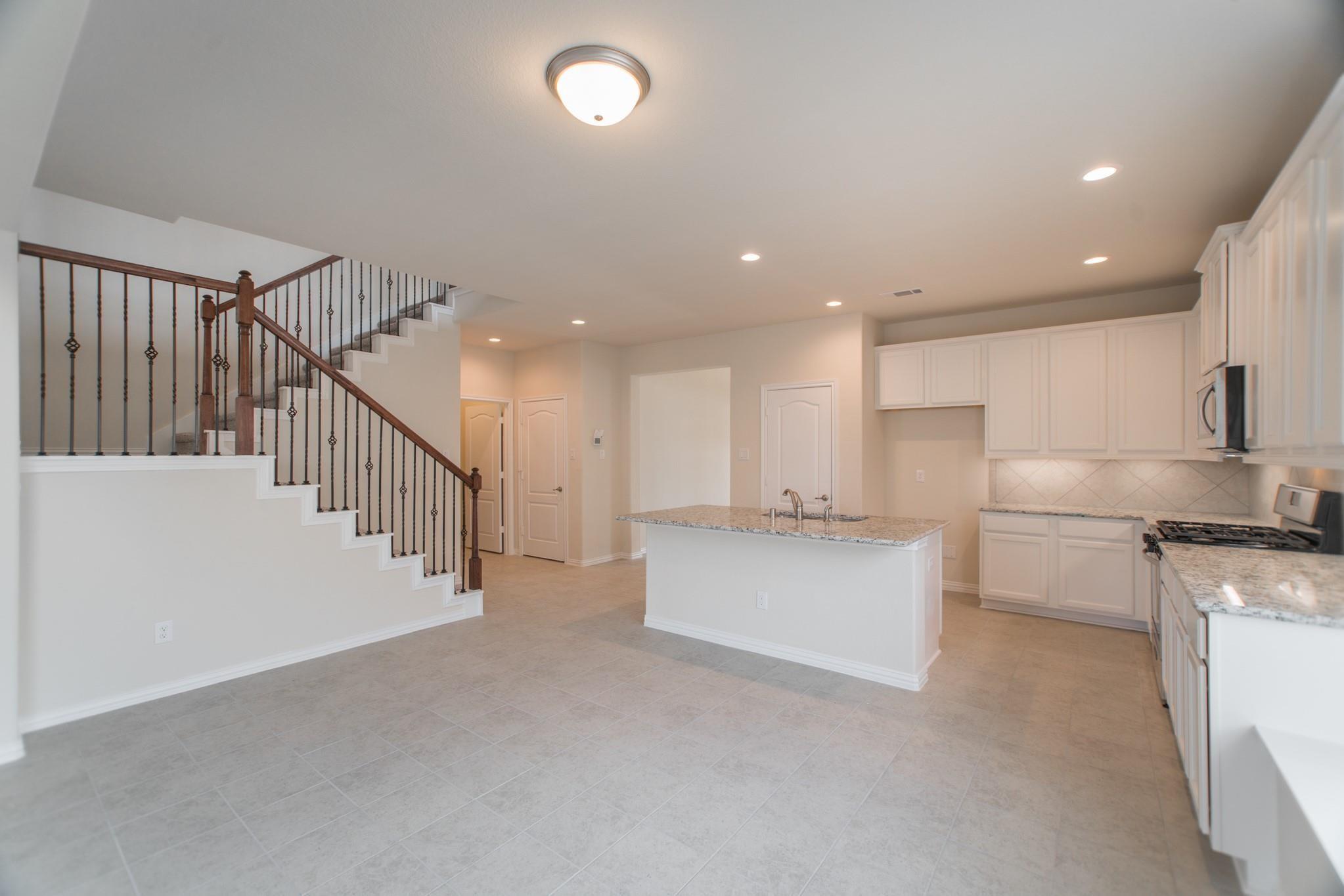 Unfurnished kitchen with a granite island and a staircase with dark wood handrails.