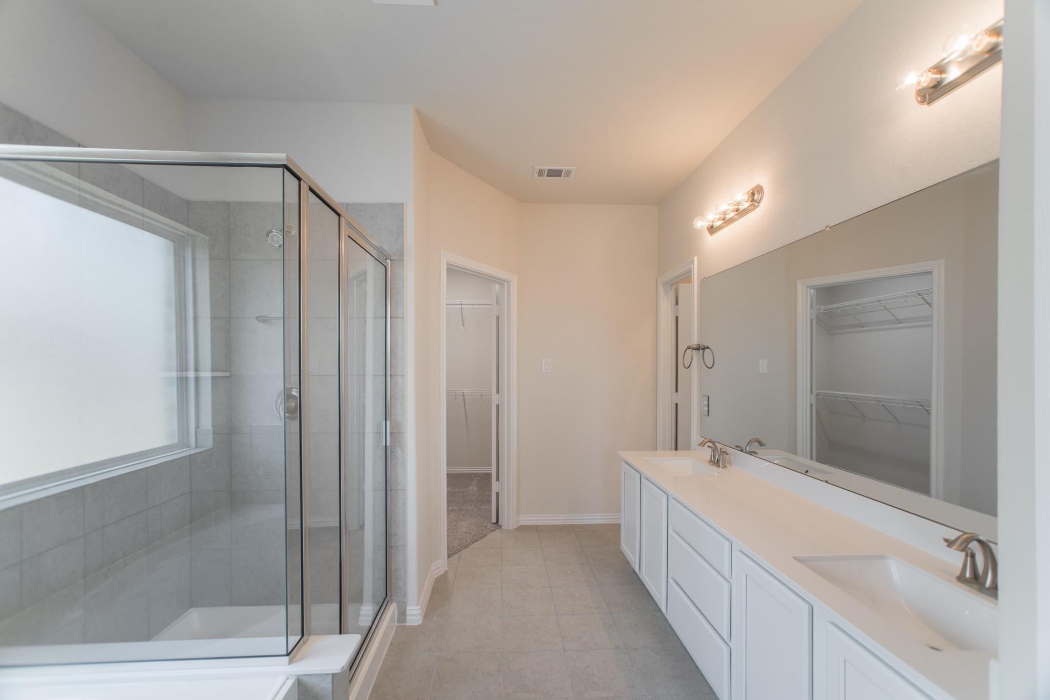Primary bathroom with double vanity, large mirror, and glass-enclosed tiled shower.