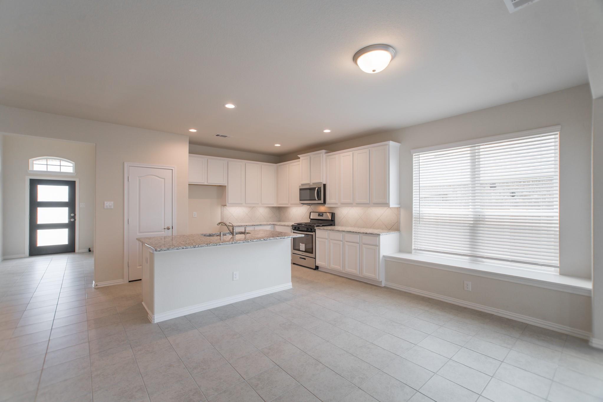 Vacant kitchen with white cabinets, a granite island, stainless steel appliances, and a large window.